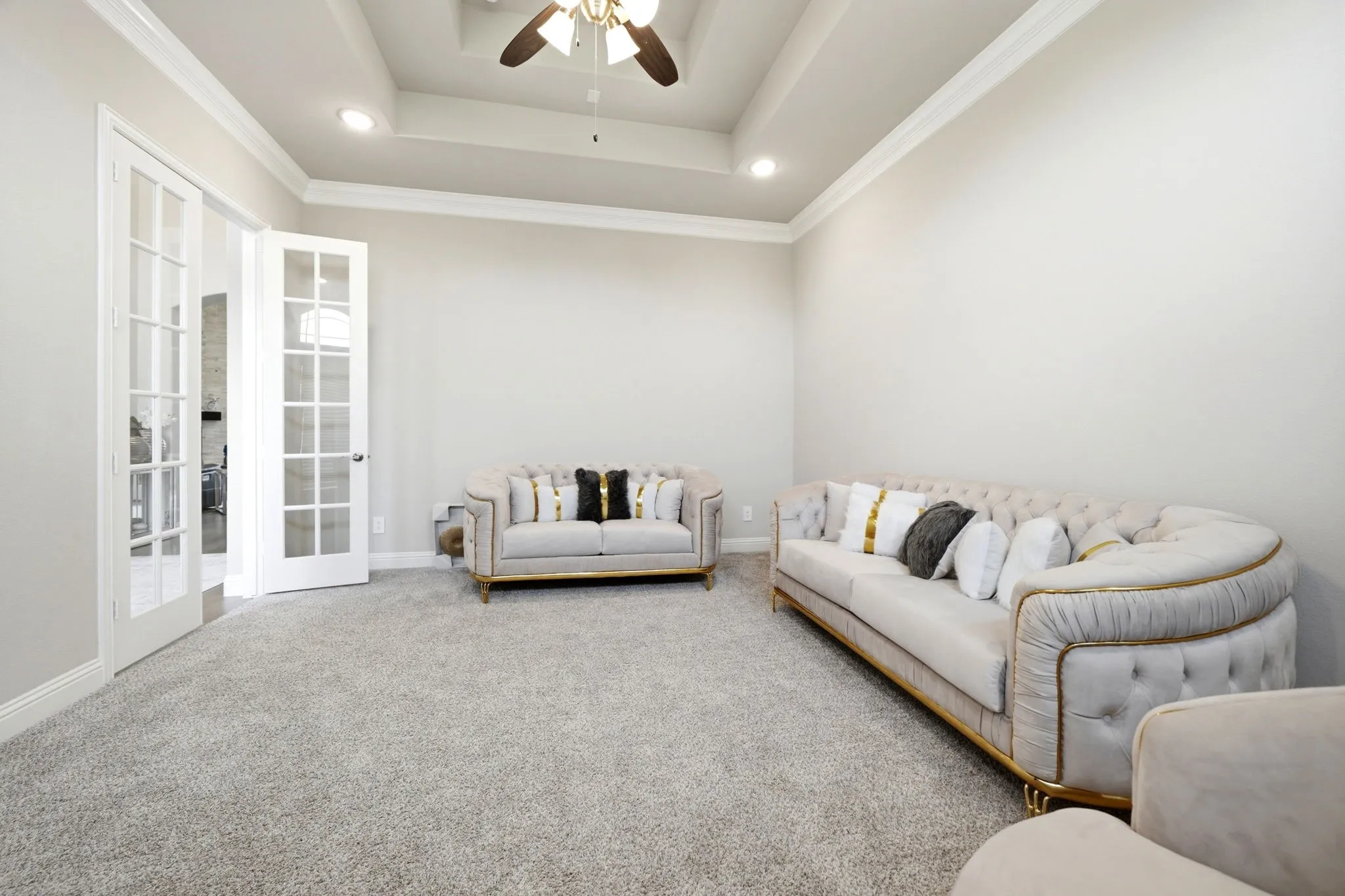 Spacious room featuring light gray carpet, crown molding, a tray ceiling with a ceiling fan, recessed lighting, and double French doors with multiple glass panes