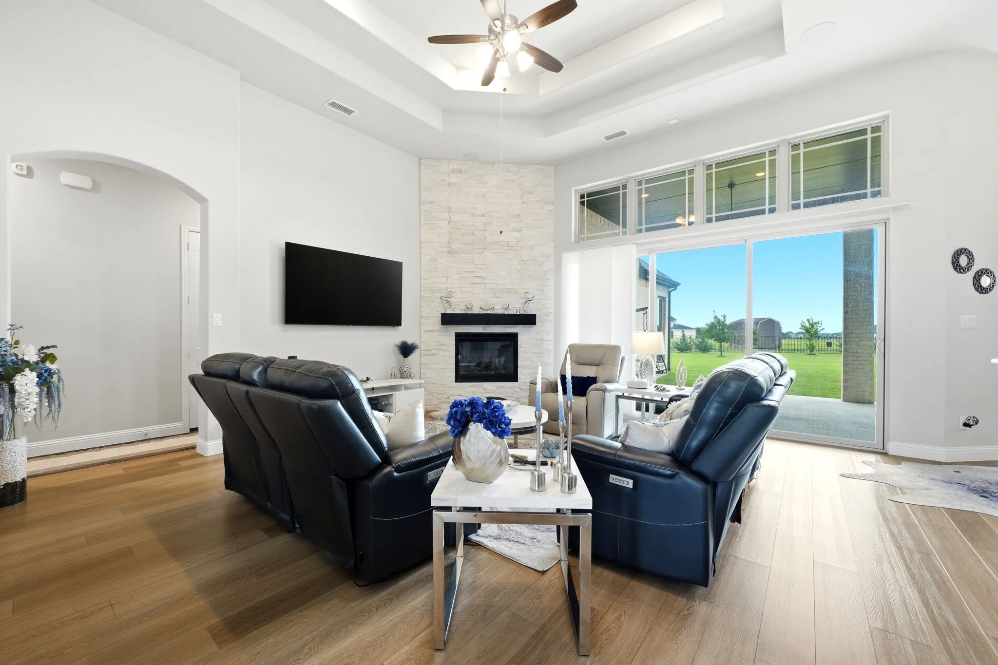 Spacious living area featuring wood-finish flooring, a tiered tray ceiling with a ceiling fan, and an arched entry