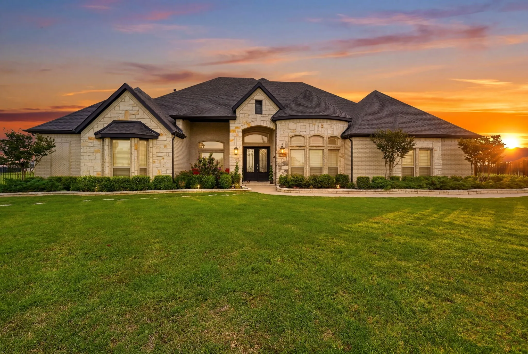 Stone facade exterior featuring a dark shingle roof and a spacious front lawn