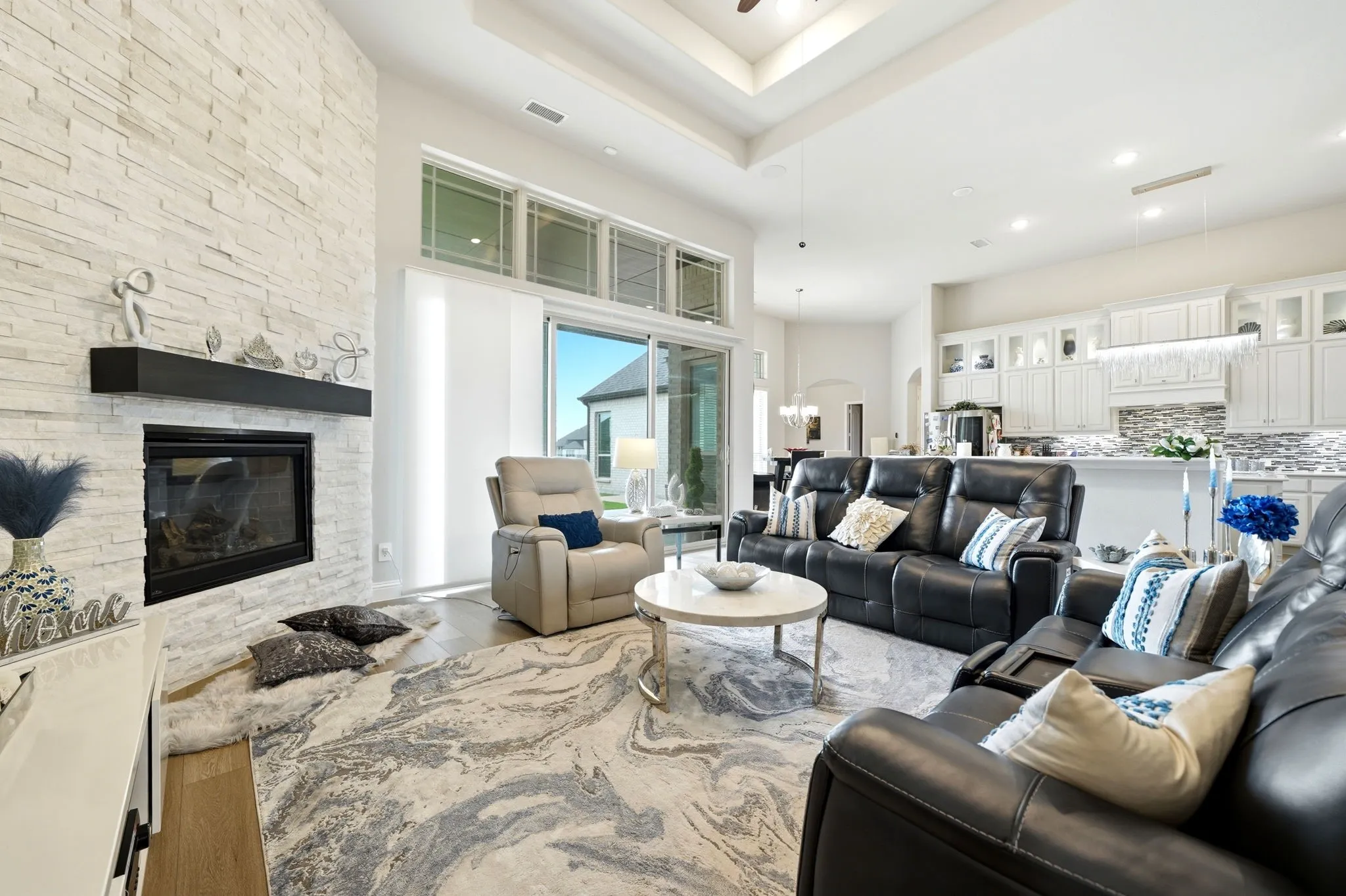 Spacious living area featuring a stacked stone fireplace with a dark wood mantel, high ceilings with a tray detail, and wood-finish flooring