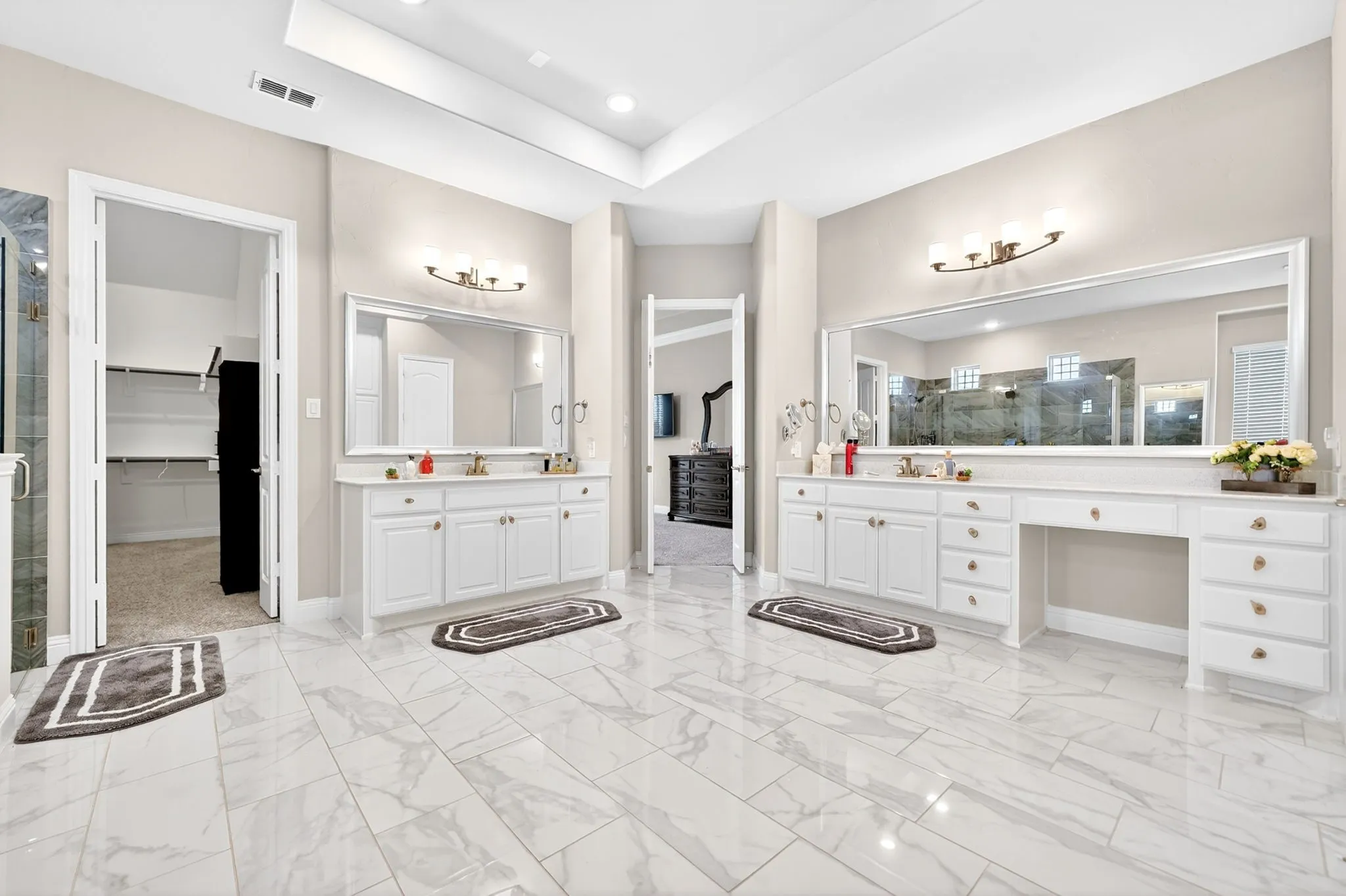 Spacious bathroom featuring marble-look tile flooring, dual white vanities with integrated sinks, large mirrors, and contemporary wall sconces