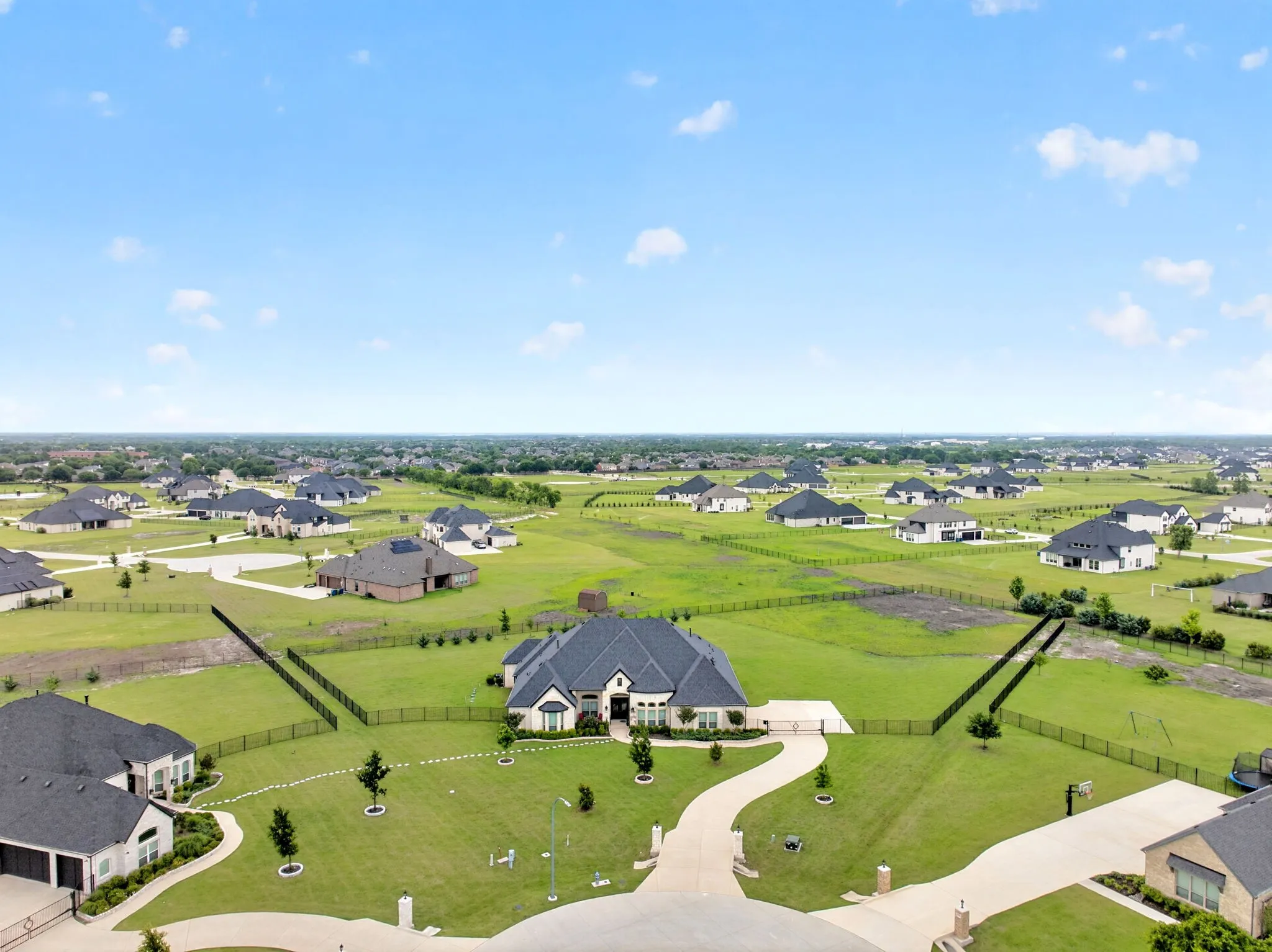 Expansive residential property featuring a large home with a dark roof and light exterior, set on a manicured green lawn