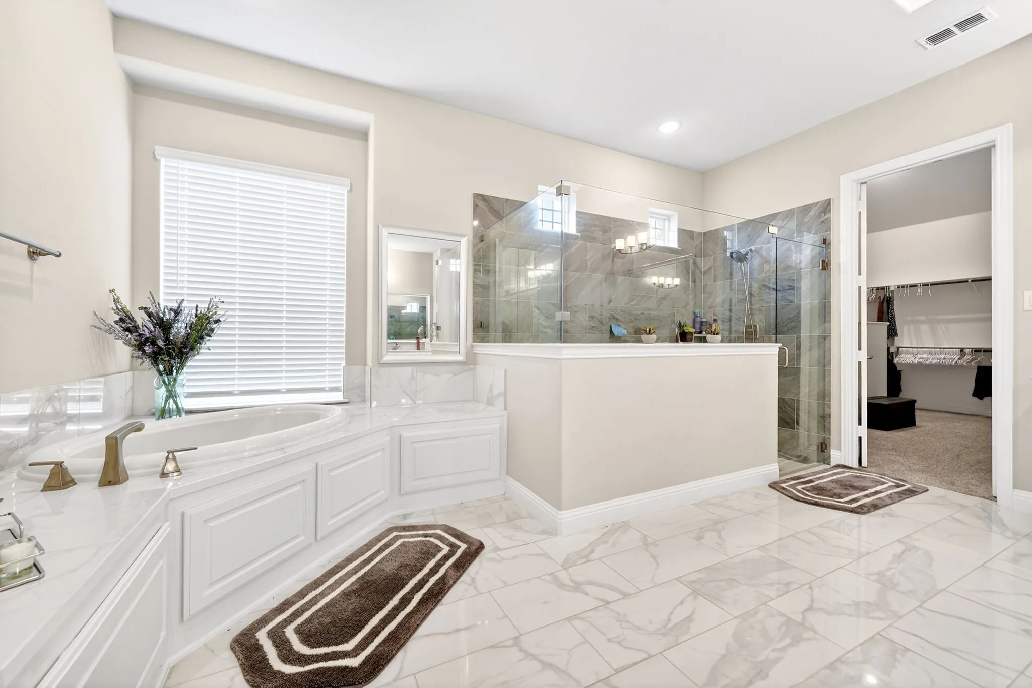 Soaking tub with brass-finish fixtures and panel detailing, set against a window with horizontal blinds
