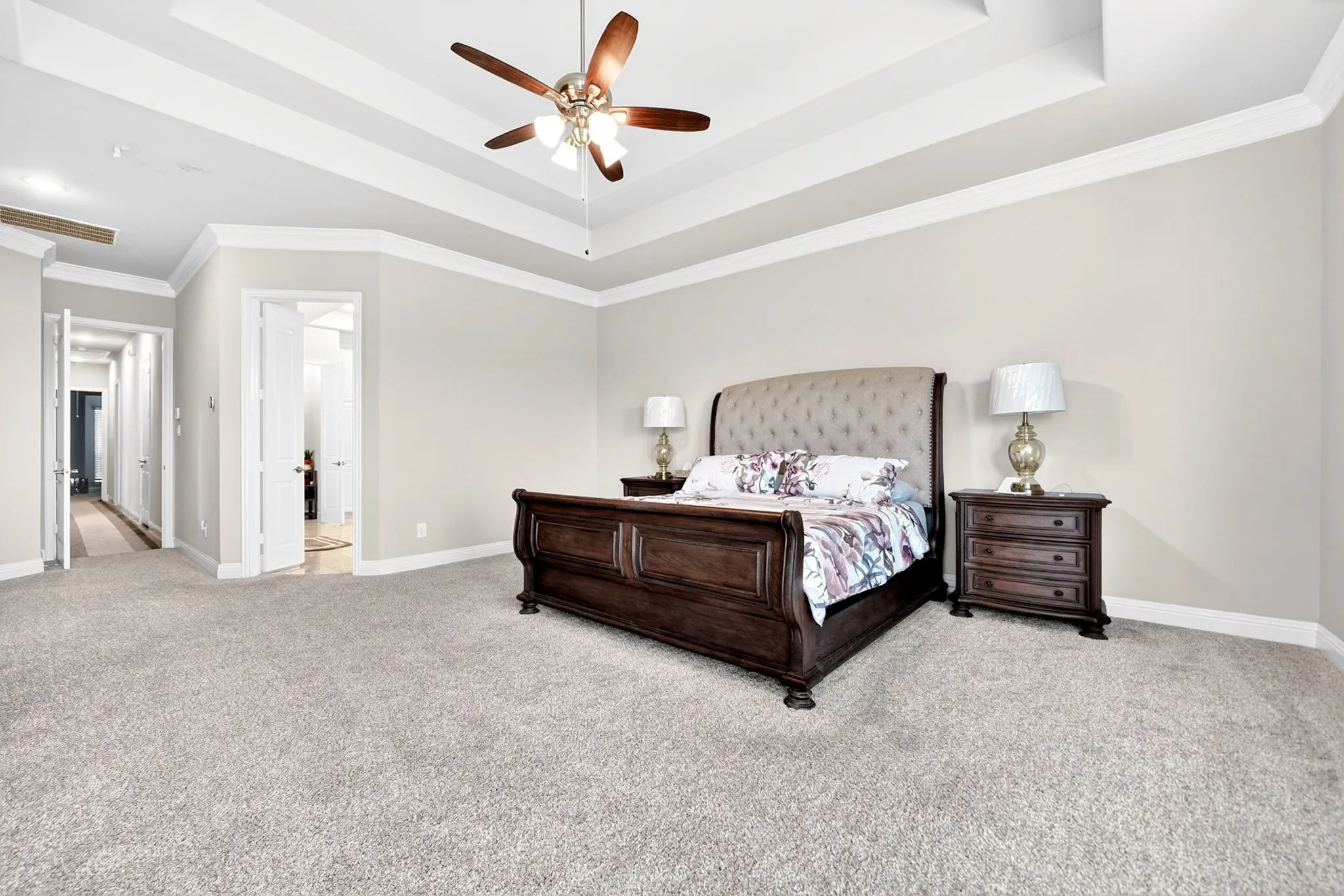 Spacious bedroom featuring light-toned carpeting and a multi-tiered tray ceiling with a ceiling fan