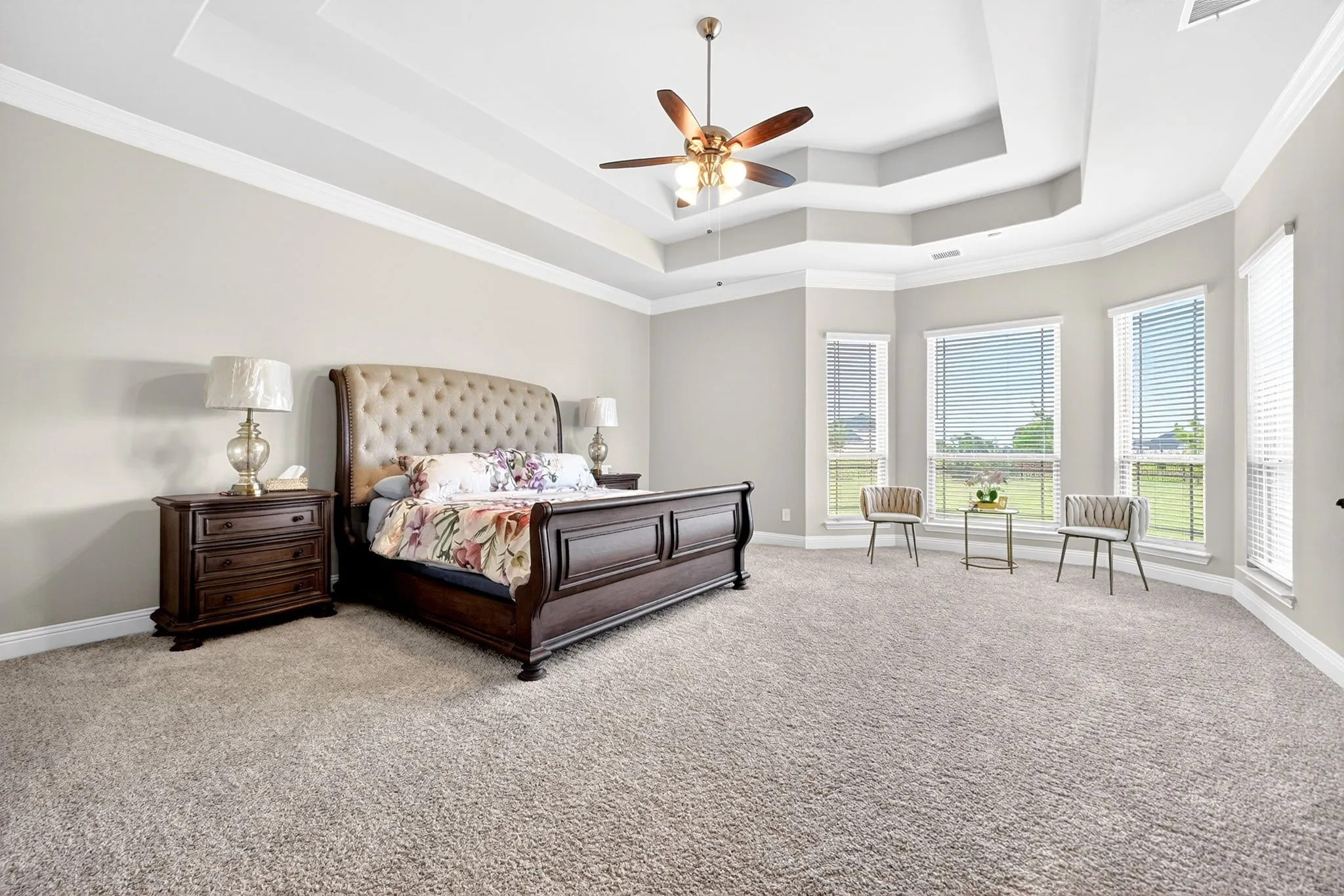 Spacious room featuring a tiered tray ceiling with crown molding, ceiling fan, and light-toned carpet flooring