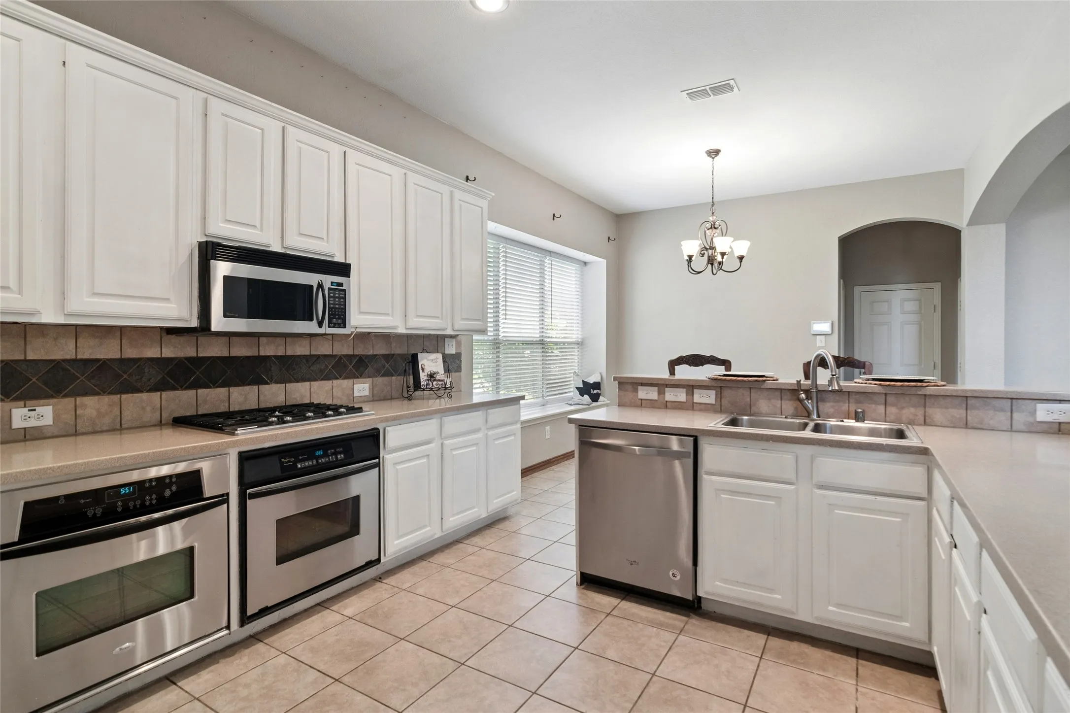 Kitchen with stainless appliances, double ovens, gas cooktop, white cabinetry, breakfast bar open to family room.