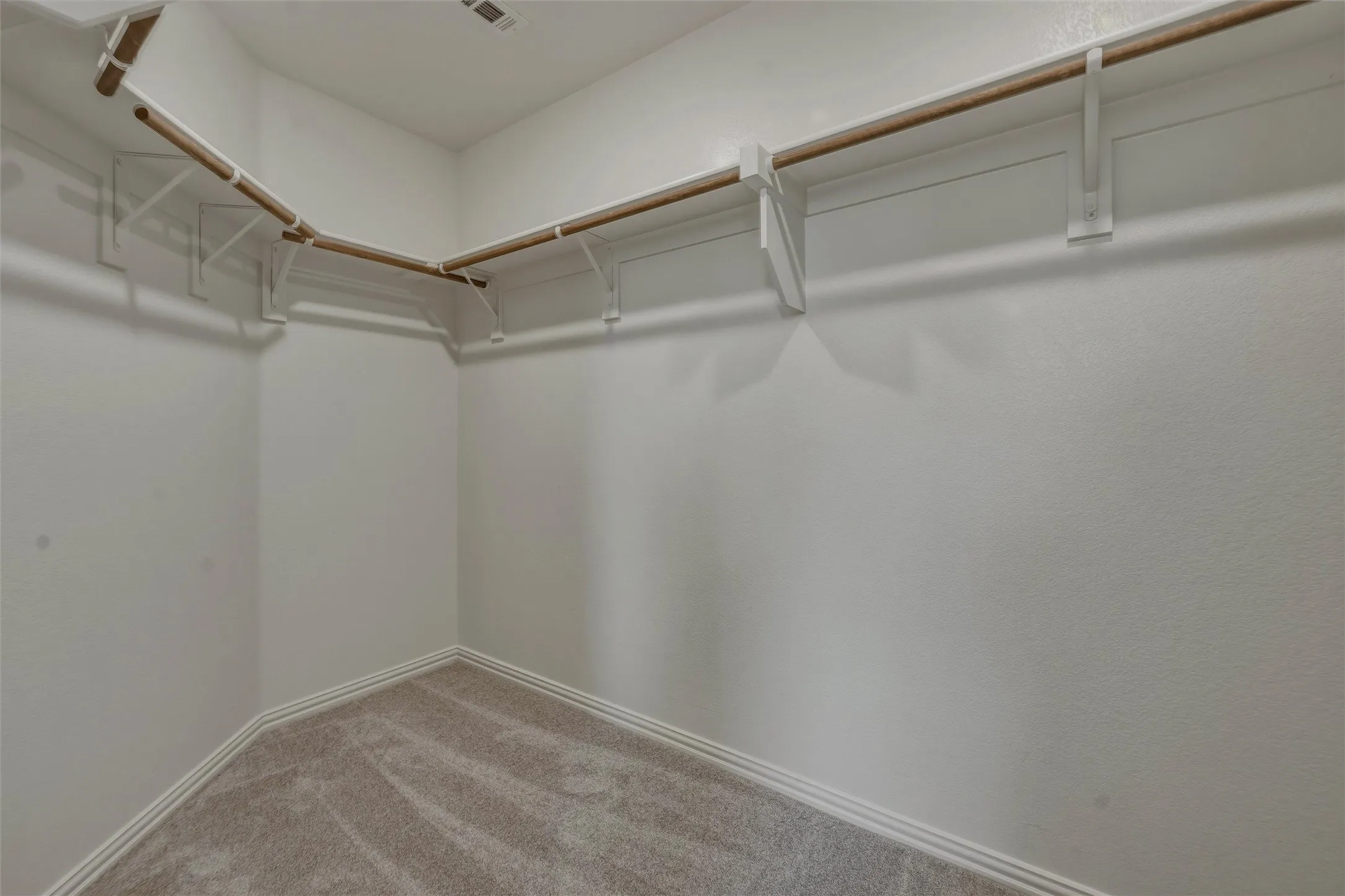 Walk-in closet featuring light beige carpet flooring, white baseboards, white textured walls, and a multi-level wood rod and shelving system