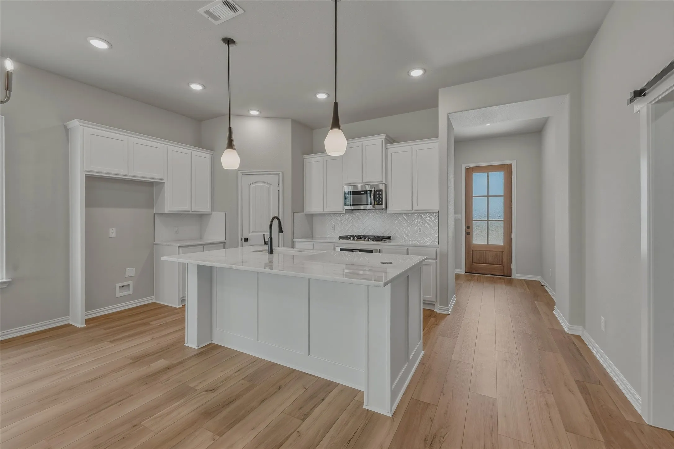 Modern kitchen featuring an island with a light-toned countertop, white cabinetry, wood-finish flooring, and recessed lighting