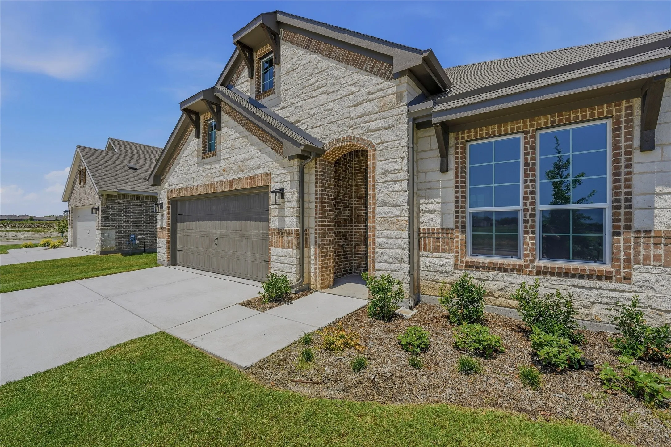 Stone and brick facade with dormer accents, archway entry, two-car garage, and multiple window placements