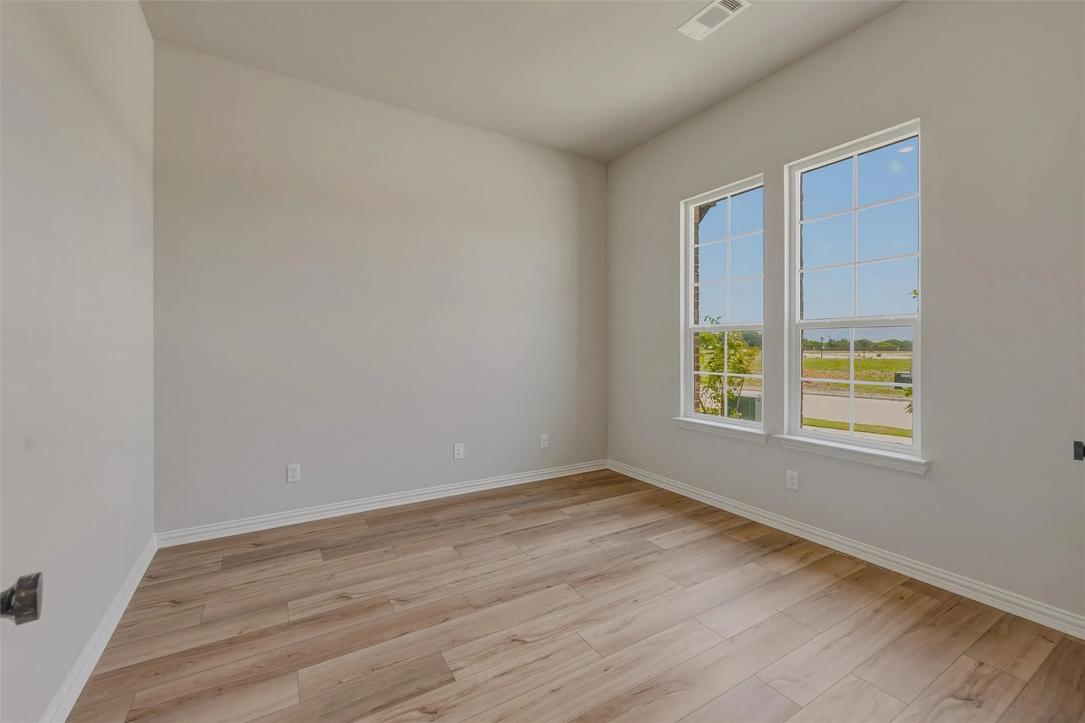 Room featuring two large windows, wood-finish flooring, light gray walls, and white baseboards