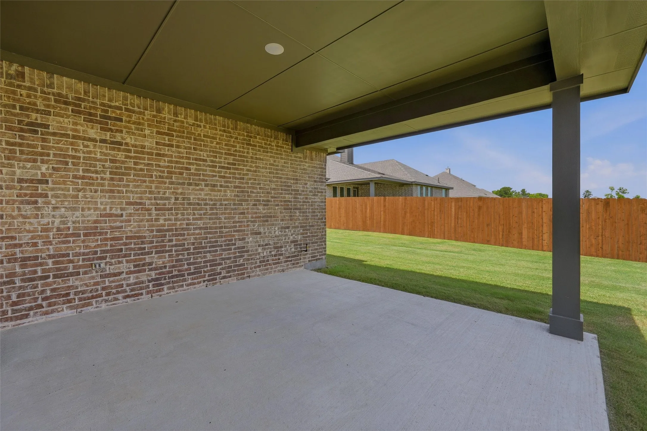 Covered patio with a concrete slab, brick exterior, flat panel soffit, and a wood privacy fence