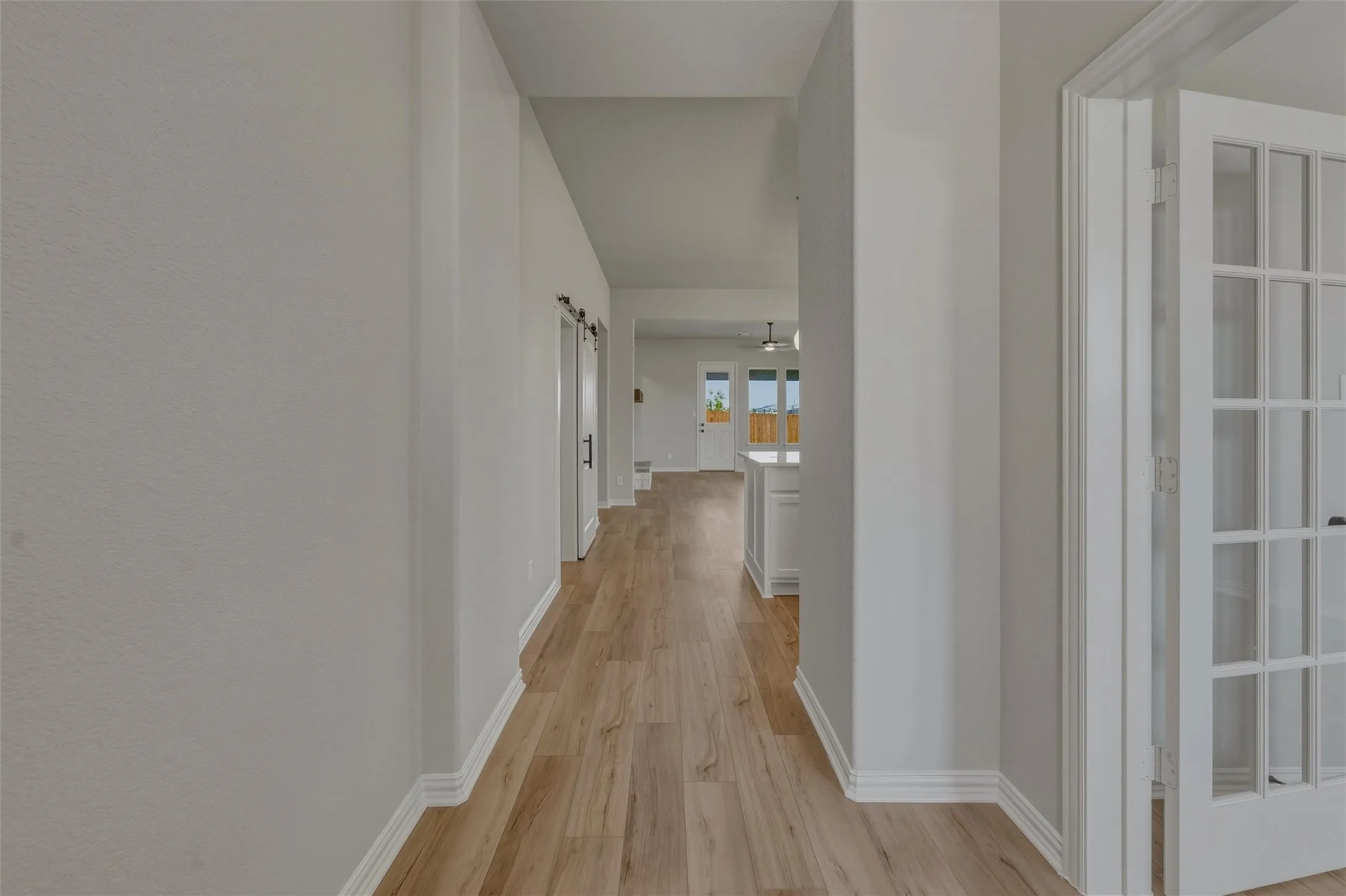 Long hallway featuring wood-finish flooring extending into the background, white baseboards, and light gray walls