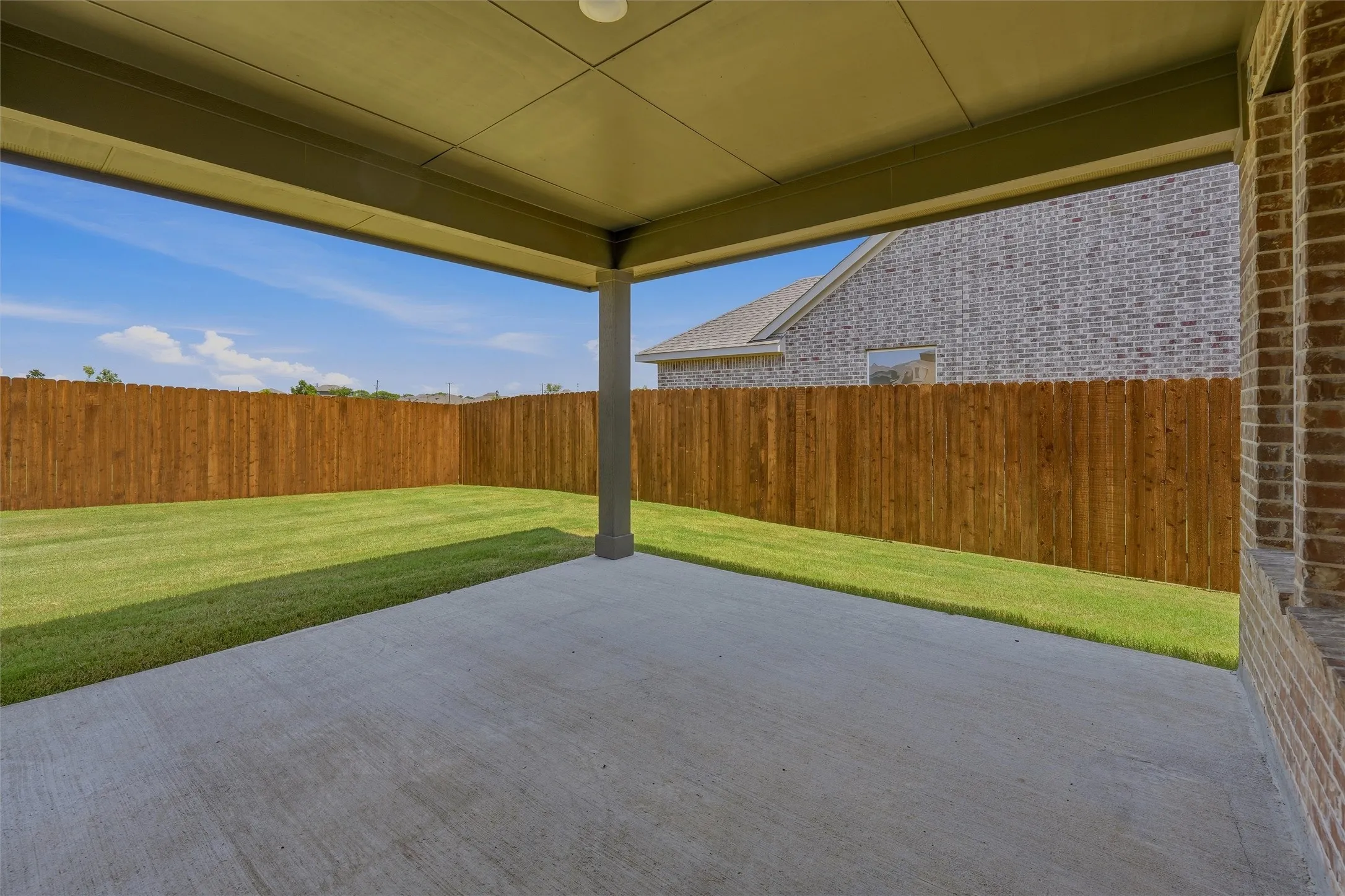 Covered patio with concrete flooring, recessed lighting, brick exterior accents, wood privacy fencing, and a manicured lawn