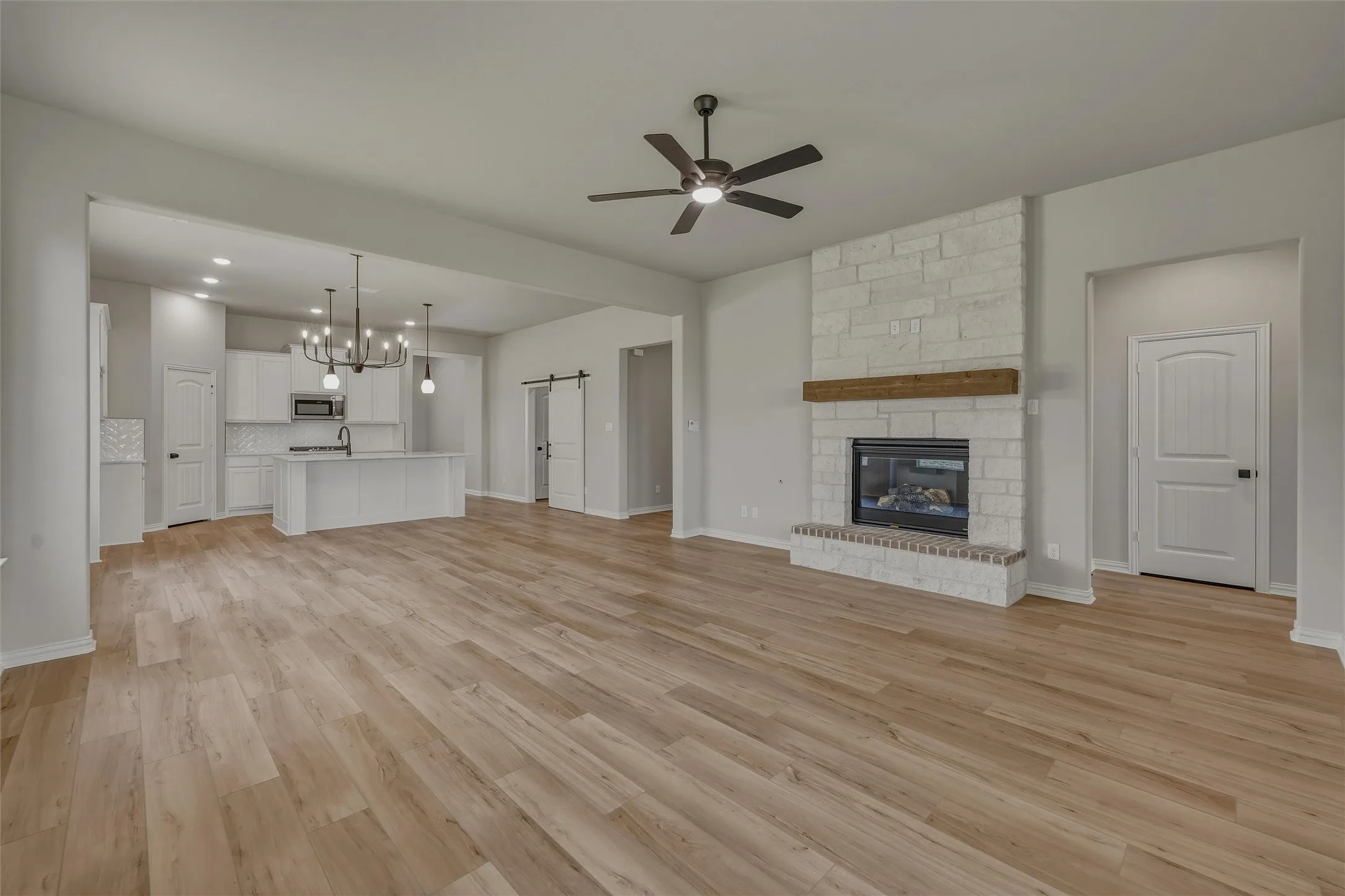 Spacious open-concept living area featuring wood-finish flooring, a stone-faced fireplace with a rustic wood mantel, and a ceiling fan