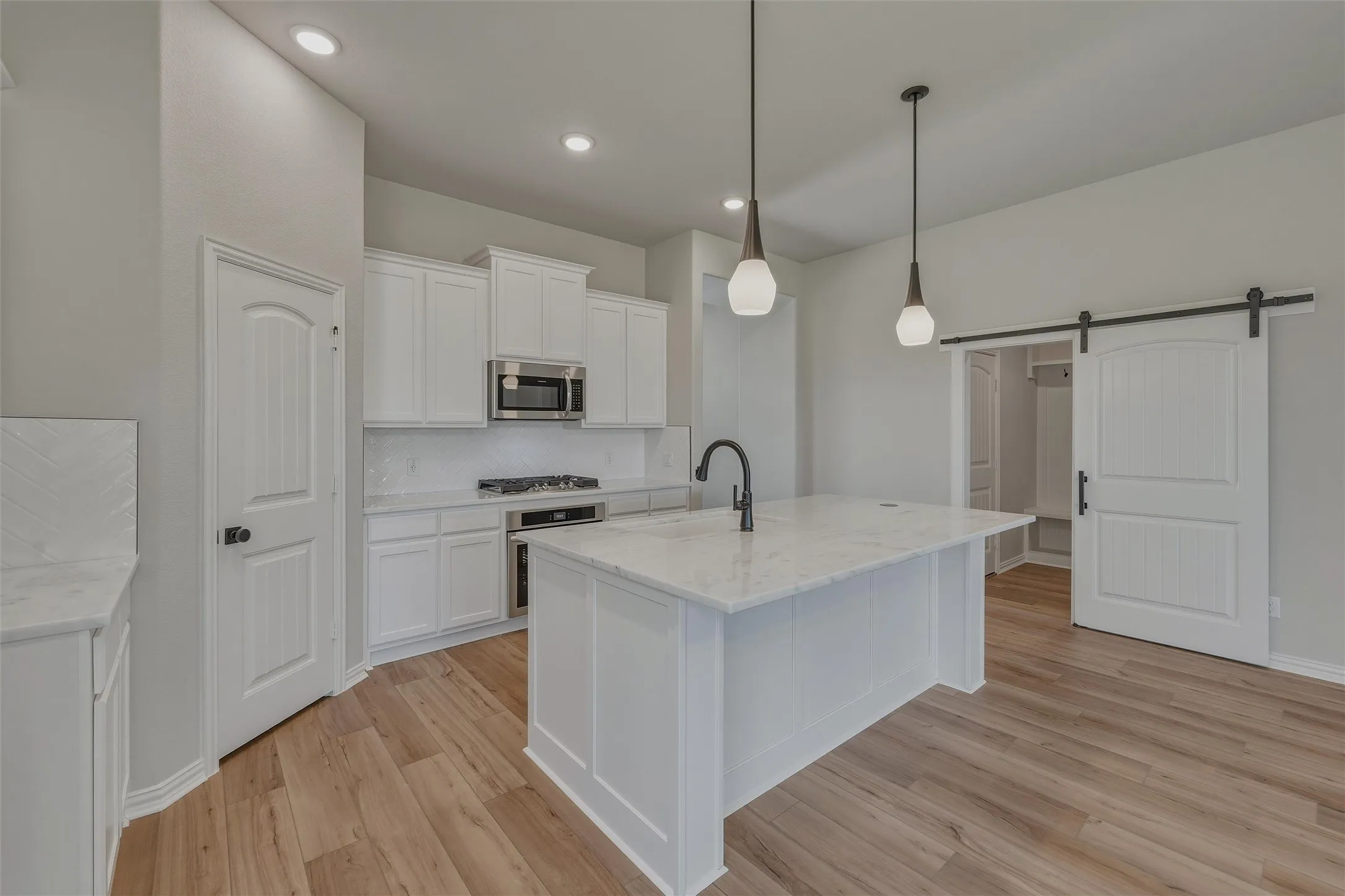 Modern kitchen featuring a central island with a light-colored countertop, white cabinetry, integrated stainless steel appliances, and wood-finish flooring