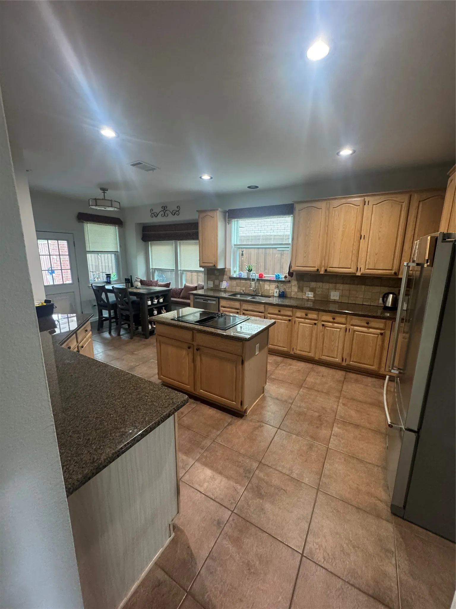 Open-concept kitchen featuring tile flooring, light wood cabinetry, granite countertops, and a central island with a built-in cooktop