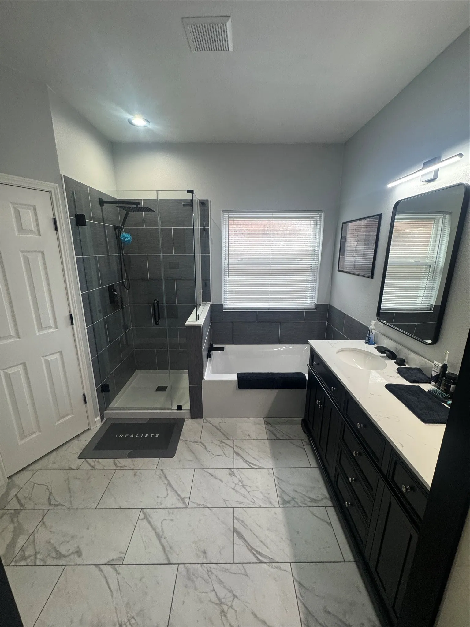 Spacious bathroom featuring a glass-enclosed shower, a separate soaking tub, and a long double vanity with stone countertop