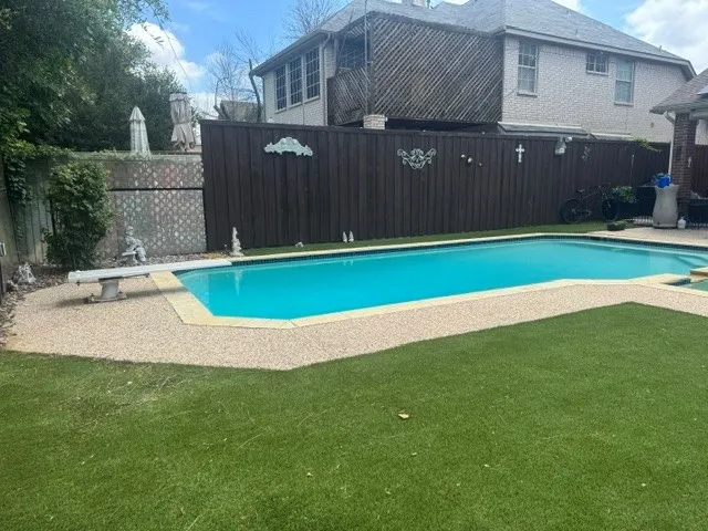 In-ground swimming pool featuring a diving board, surrounding aggregate concrete decking, and artificial turf
