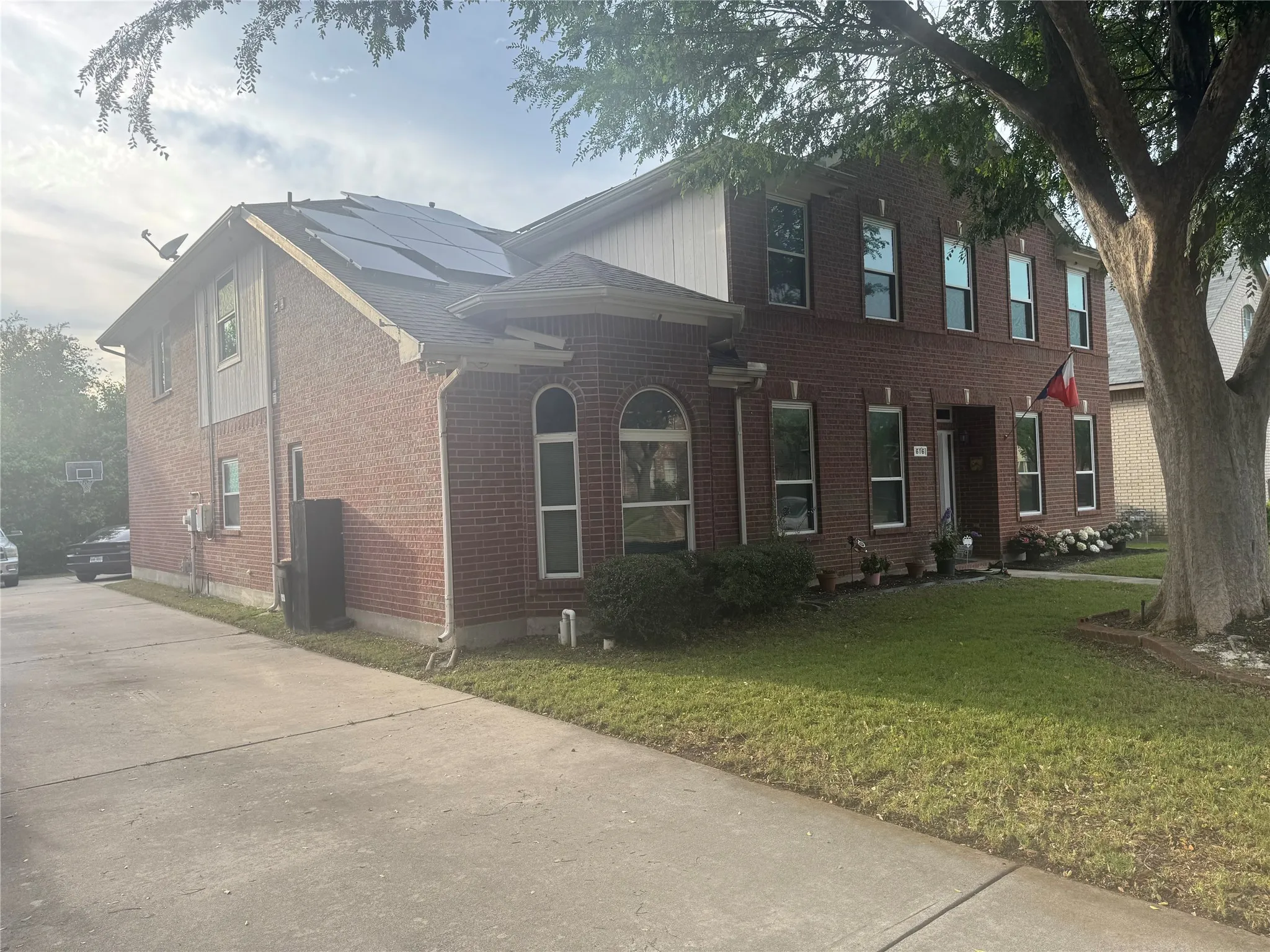 Brick exterior residence featuring solar panels, a concrete driveway, a manicured lawn, and mature trees