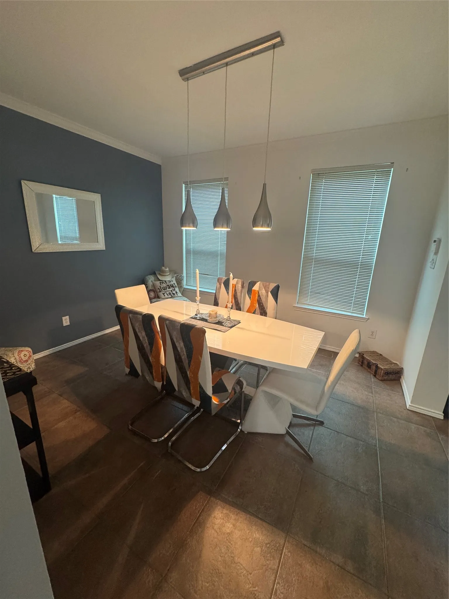 Dining area featuring a contemporary linear pendant light fixture, two windows with blinds, and tile flooring