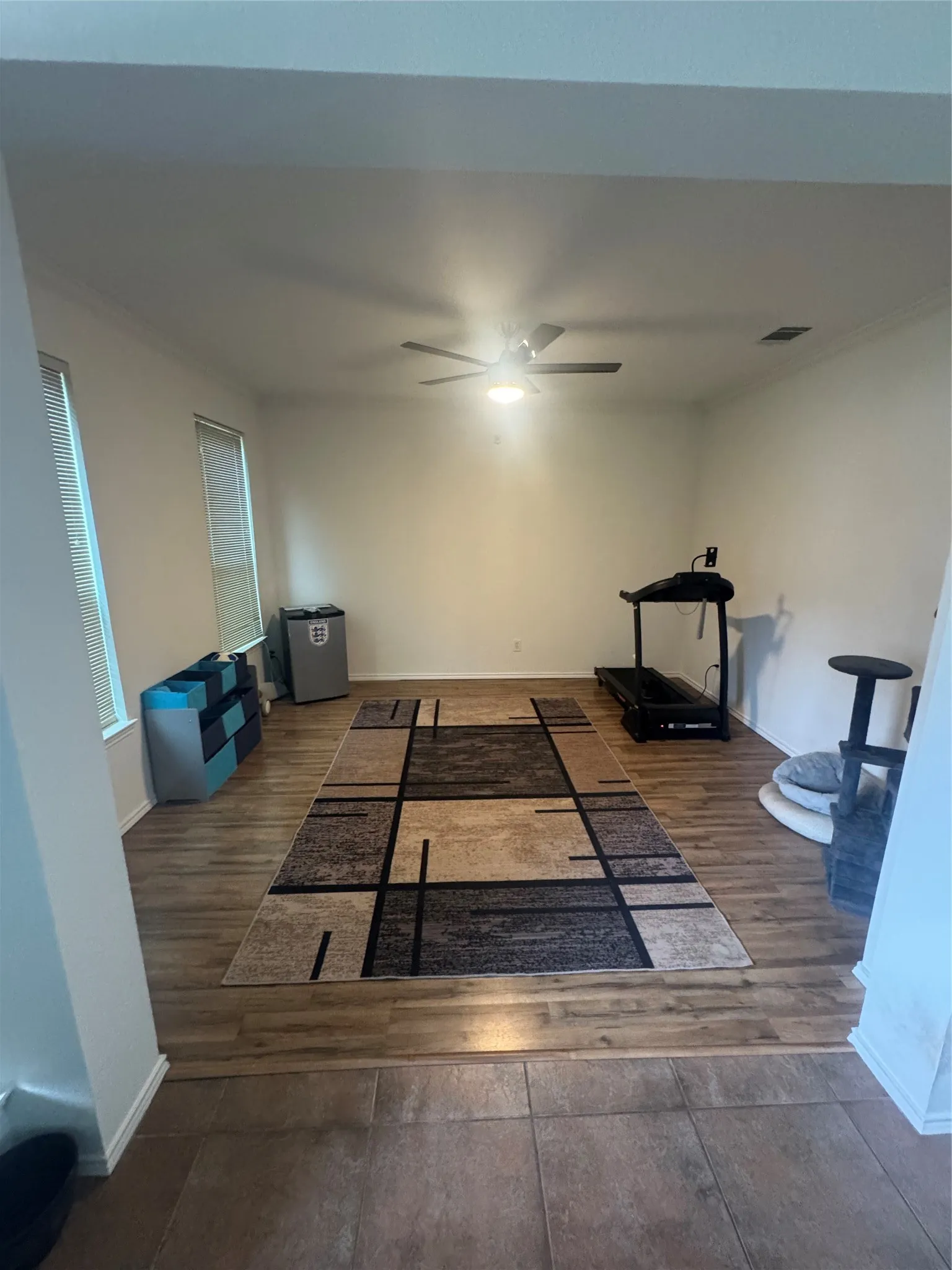 Spacious room featuring wood-finish flooring, a ceiling fan with integrated lighting, and multiple windows with blinds