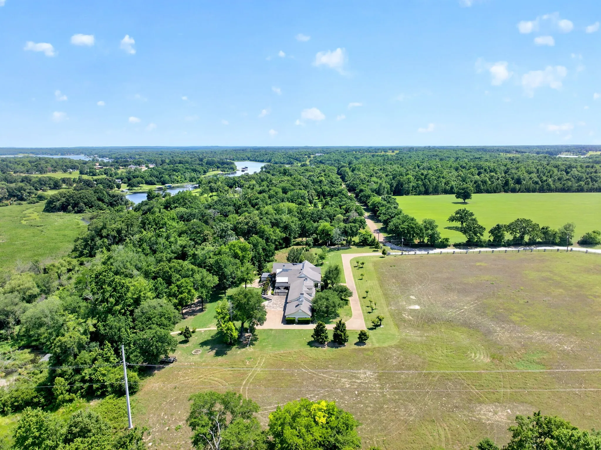 Spacious property featuring a large residence with an attached garage, extensive surrounding greenery, mature trees, and a distant body of water