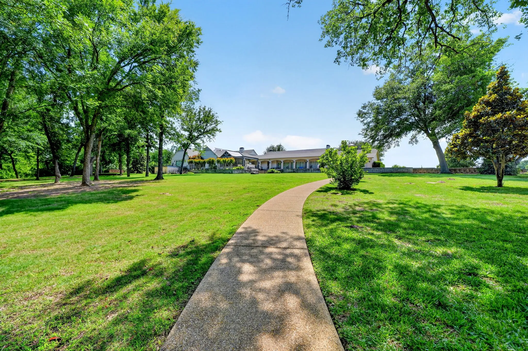 Spacious lawn with a winding concrete pathway, mature trees, and landscaping