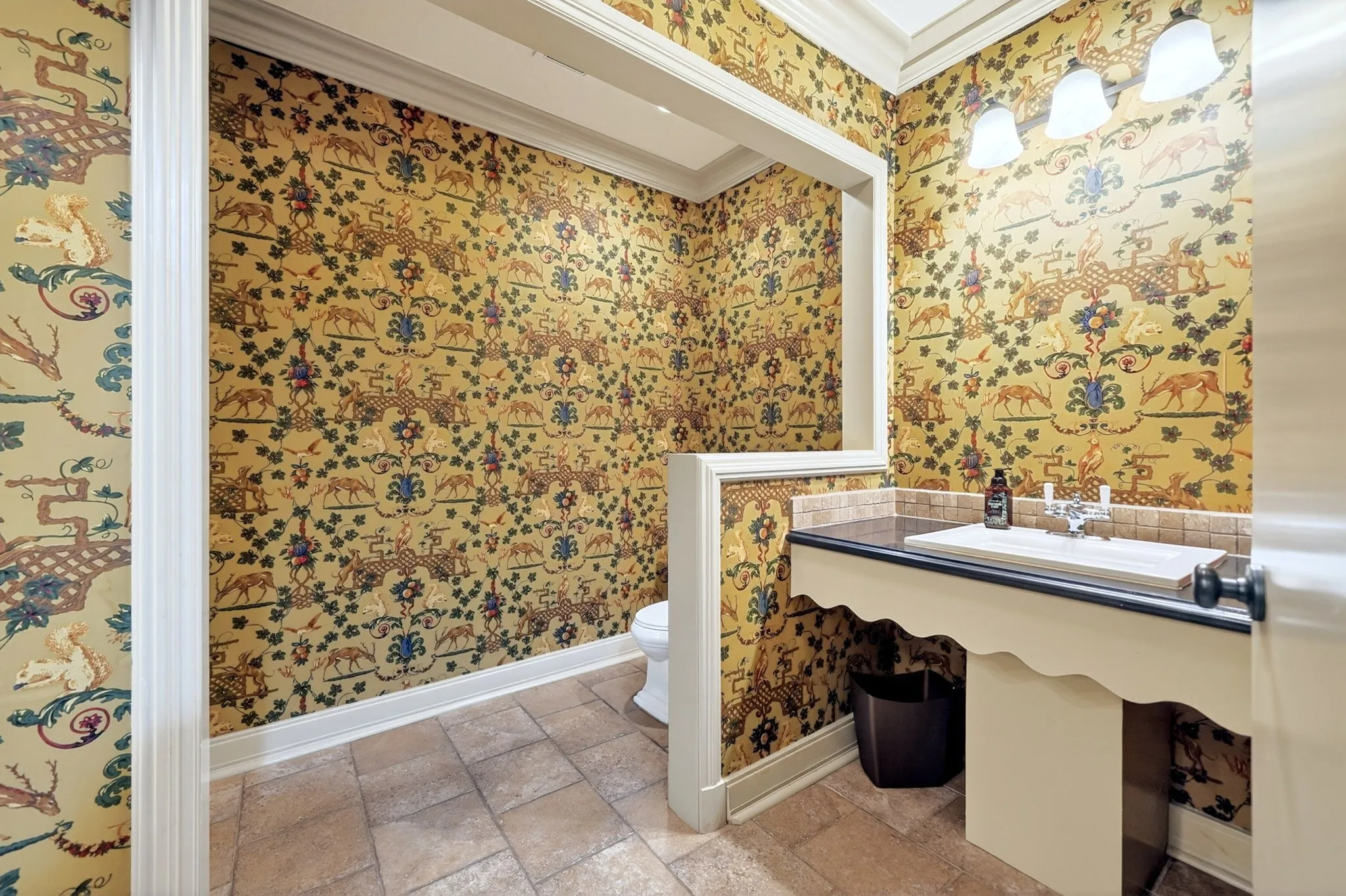 Powder room featuring detailed patterned wallpaper, a bespoke vanity with an integrated sink, a dark countertop, and a tiled backsplash