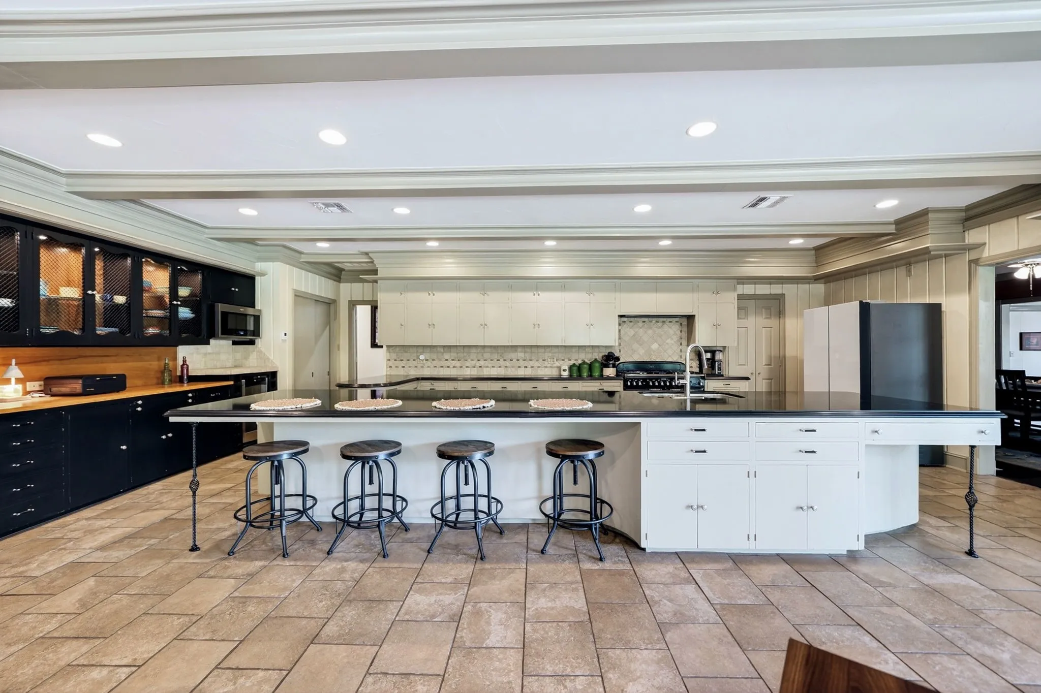 Kitchen featuring a large central island with seating, dark countertops, built-in cabinetry, recessed lighting, and tile flooring