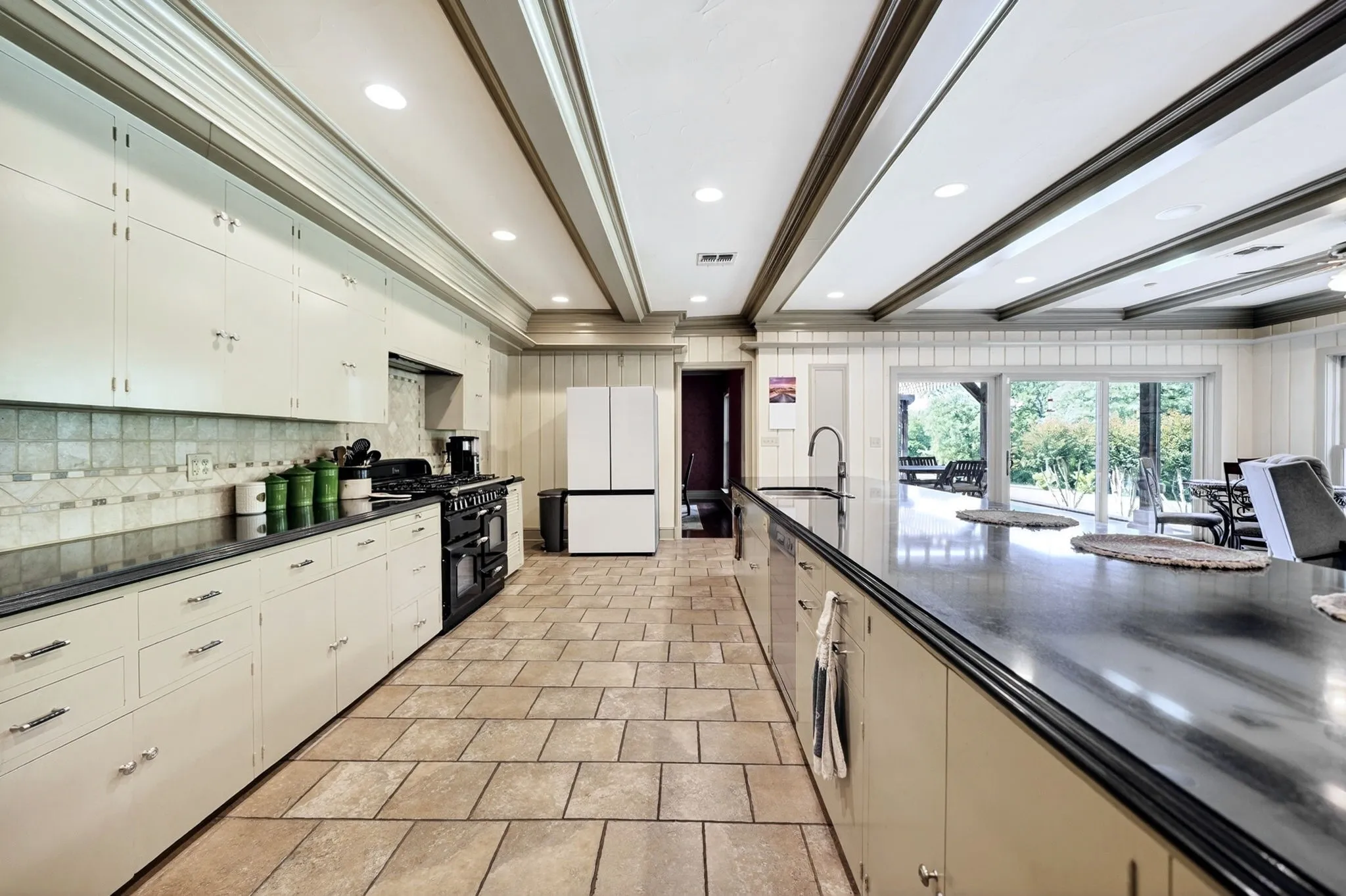 Spacious kitchen featuring extensive cabinetry, dark countertops, tiled flooring, recessed lighting, and a large central island with an integrated sink