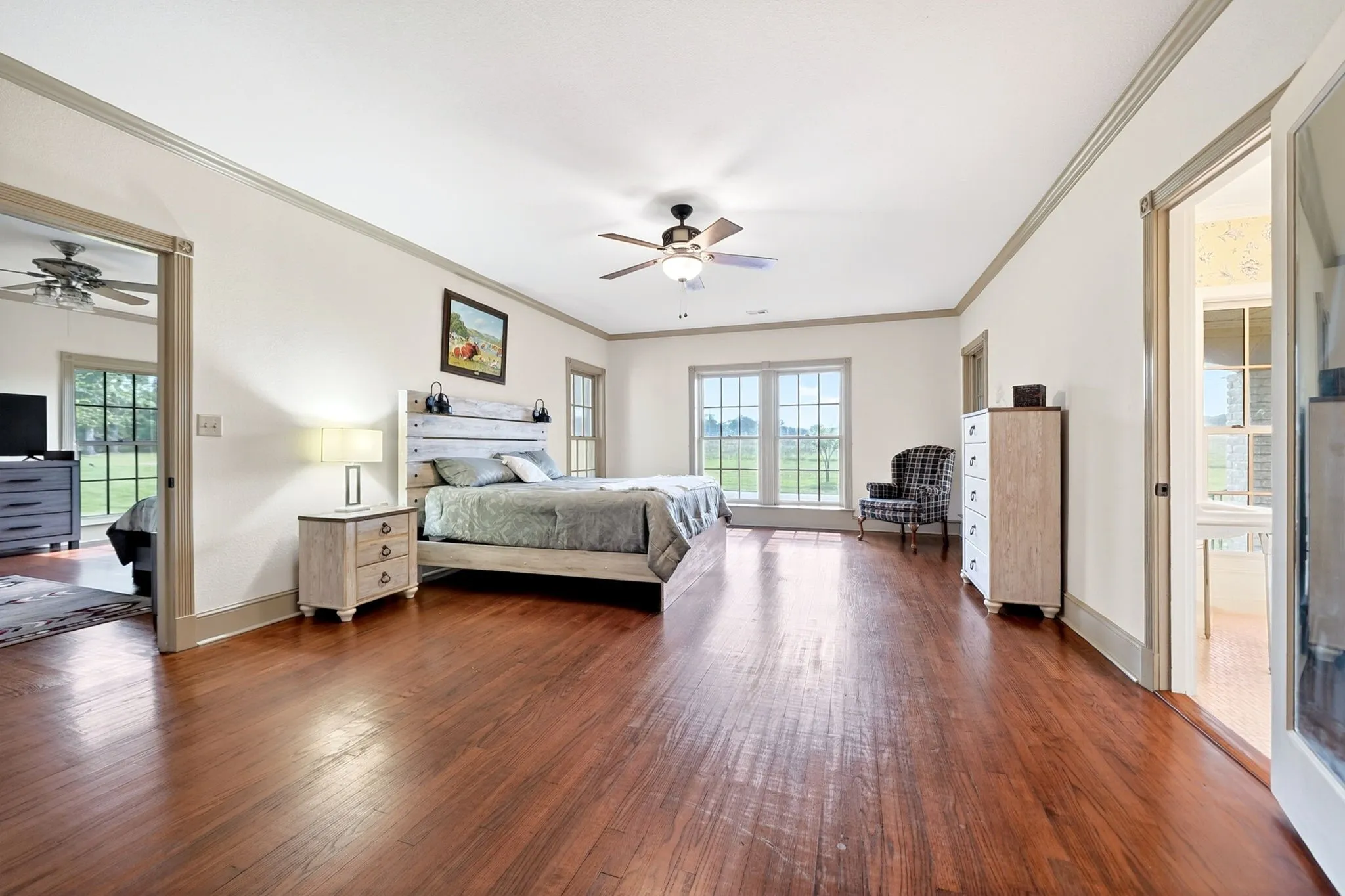 Spacious room featuring rich wood-finish flooring, a ceiling fan, and white walls with gray trim