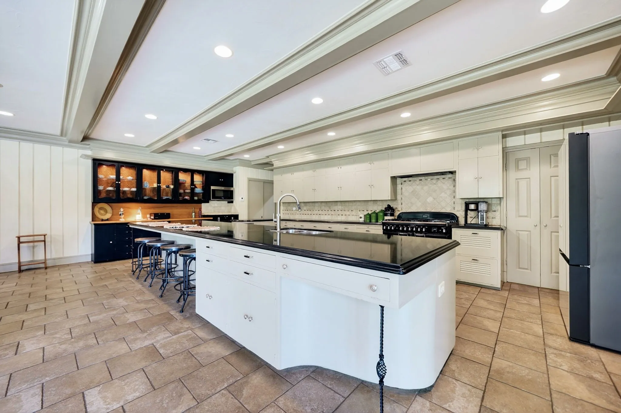 Spacious kitchen featuring a large central island with a sink and seating, white cabinetry, integrated range, tile flooring, and coffered ceilings with recessed lighting
