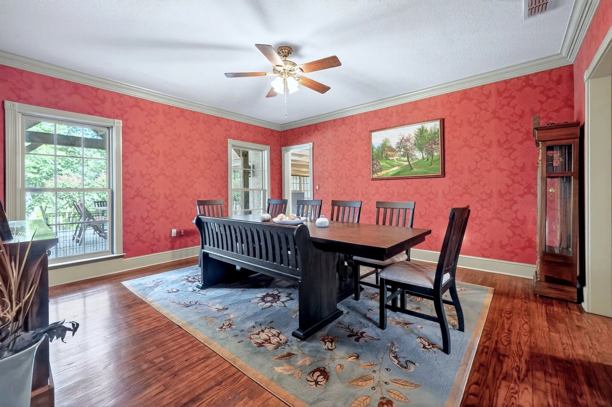 Formal dining space featuring wood-finish flooring, patterned red wall coverings, and a ceiling fan with integrated lighting