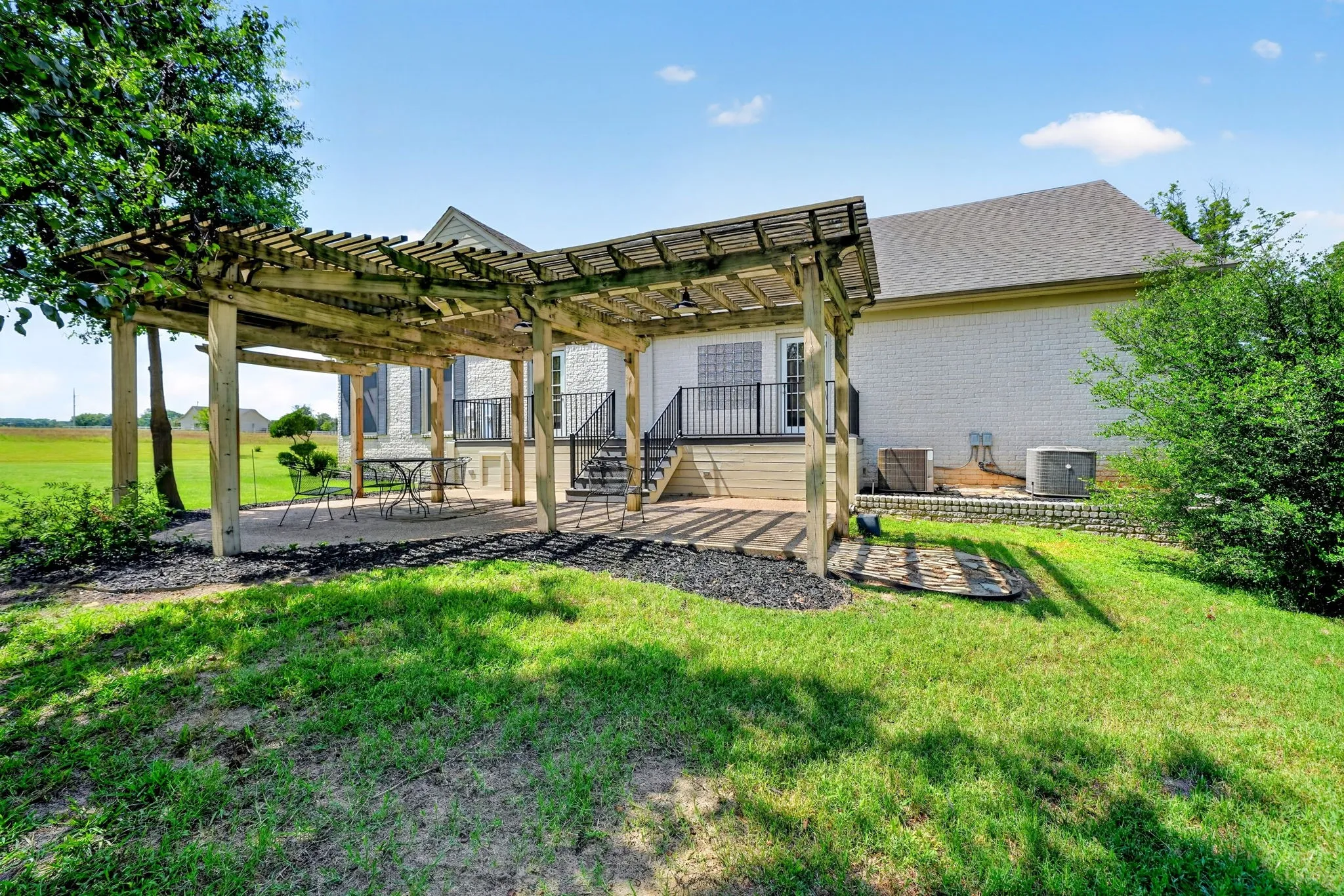 Expansive outdoor patio featuring a wooden pergola, gravel ground cover, and a staircase leading to an upper-level deck with black railings
