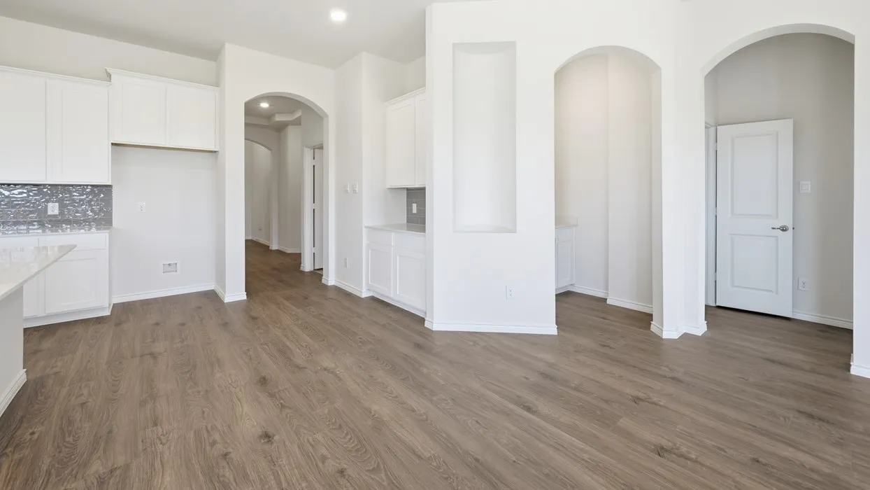 Open-concept layout featuring wood-finish flooring throughout, white cabinetry, a decorative tile backsplash, and multiple arched doorways