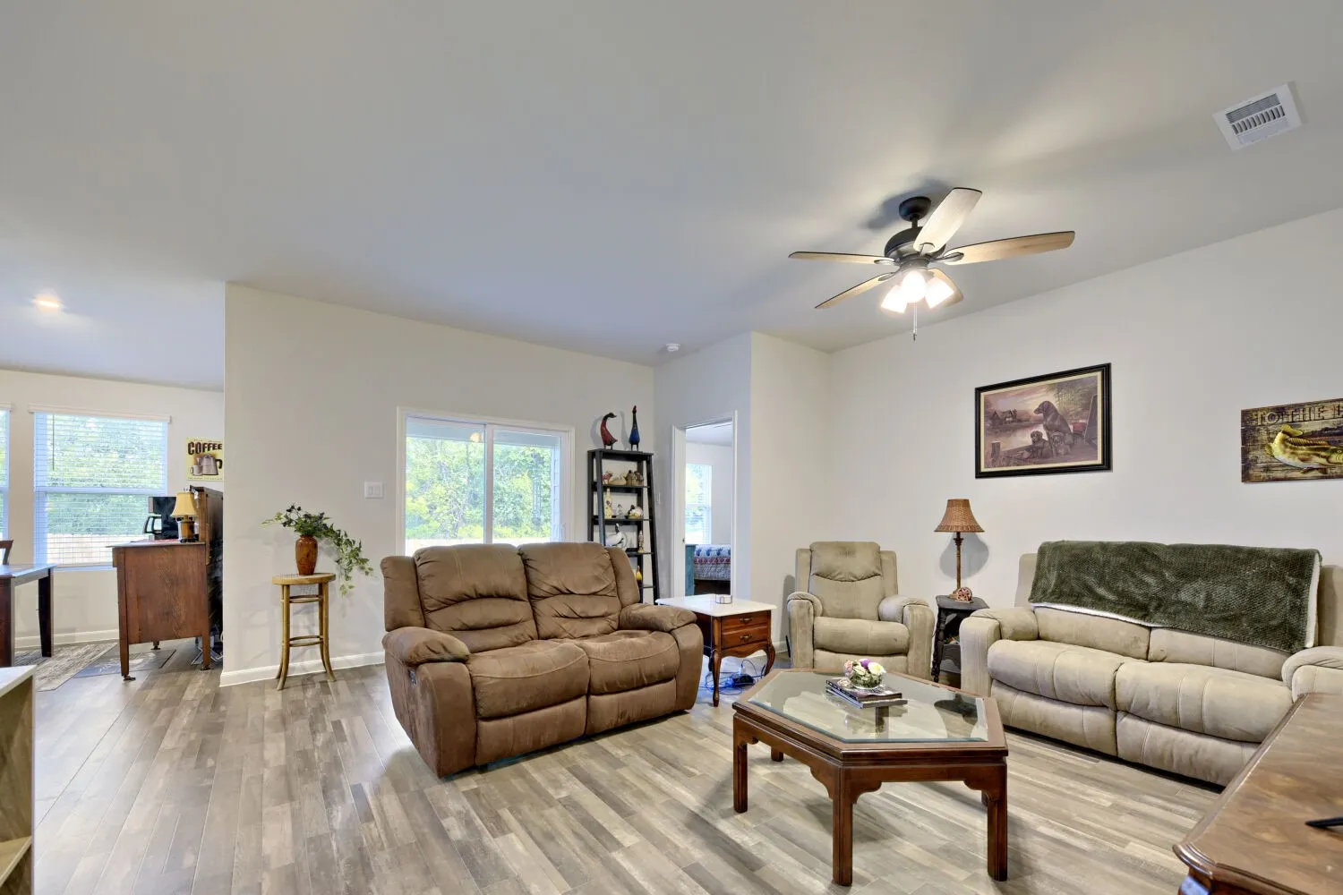 Spacious interior with wood-finish flooring, a ceiling fan with integrated lighting, and white walls