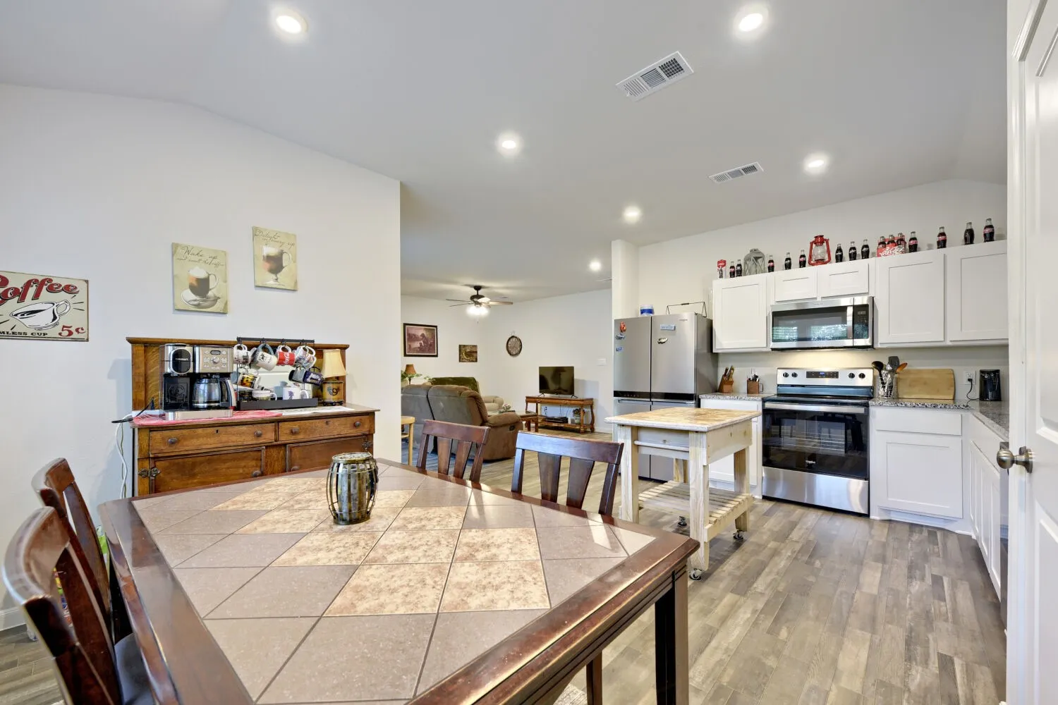 Open-concept kitchen and dining area featuring recessed lighting, wood-finish flooring, white cabinetry, stainless steel appliances, and light-toned countertops