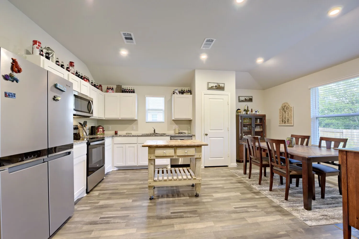 Open-concept kitchen and dining area featuring wood-finish flooring, white cabinetry, recessed lighting, and stainless steel appliances