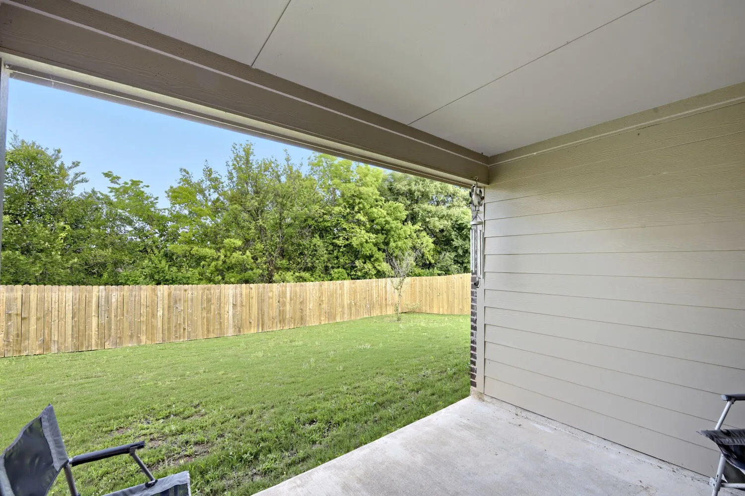 Covered concrete patio overlooking a private backyard with a wood privacy fence and mature trees