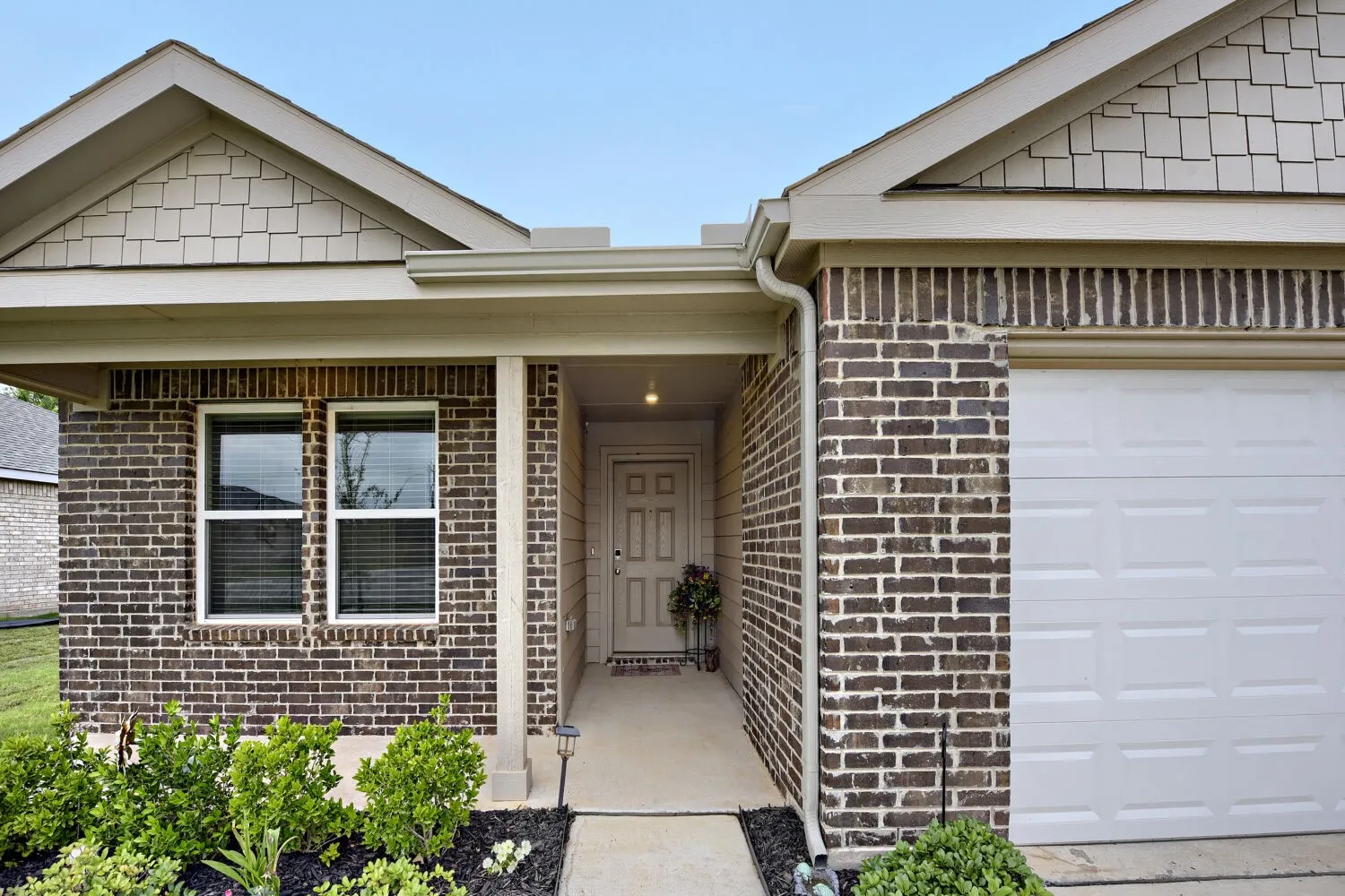 Exterior featuring a brick facade, covered entry, and attached garage