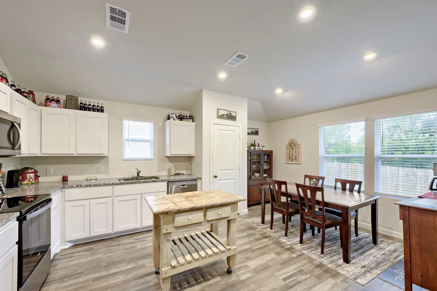Open-concept kitchen and dining area featuring wood-finish flooring, recessed lighting, white cabinetry, granite countertops, and stainless steel appliances
