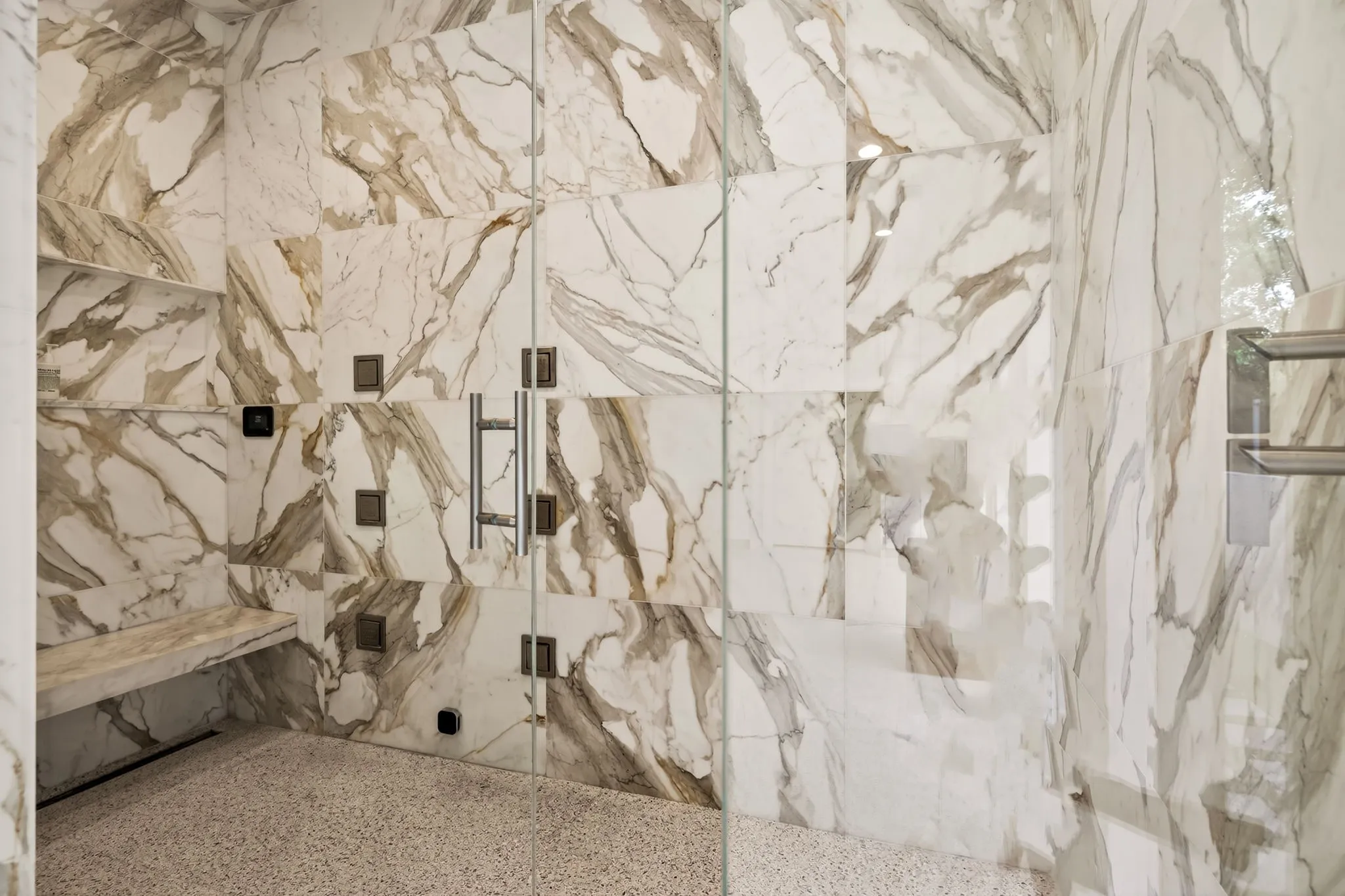Spacious shower enclosure featuring full-height stone tile walls, a built-in stone bench, and an integrated linear drain