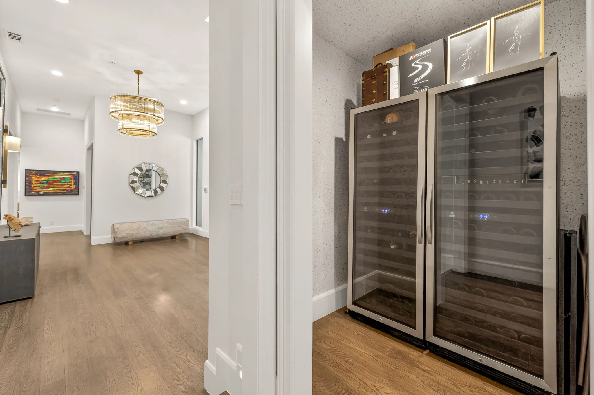 Hardwood flooring extending through a brightly lit hallway, featuring a tiered chandelier and recessed lighting