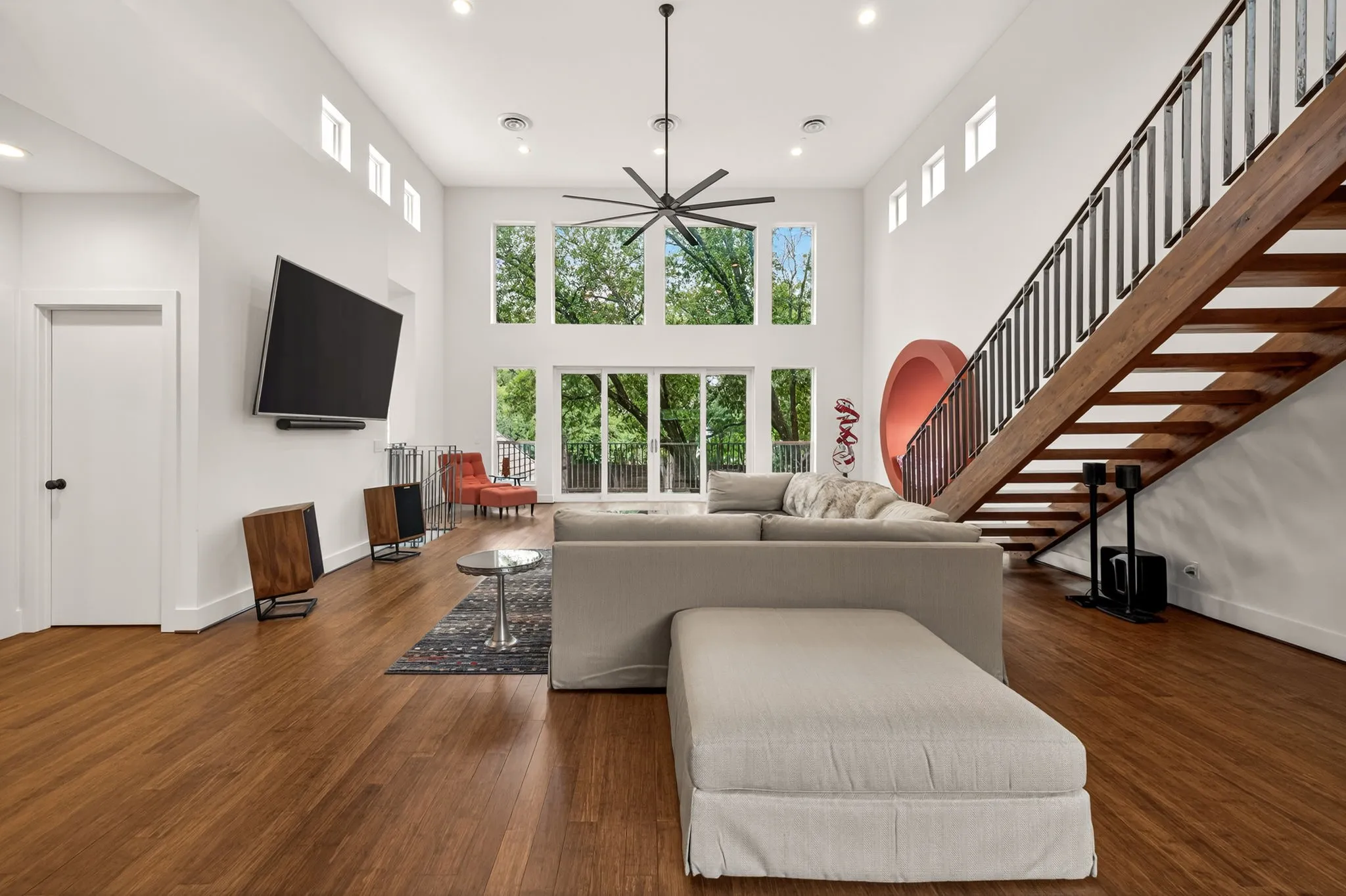 Spacious living area featuring high ceilings, wood-finish flooring, a contemporary ceiling fan, and extensive window walls