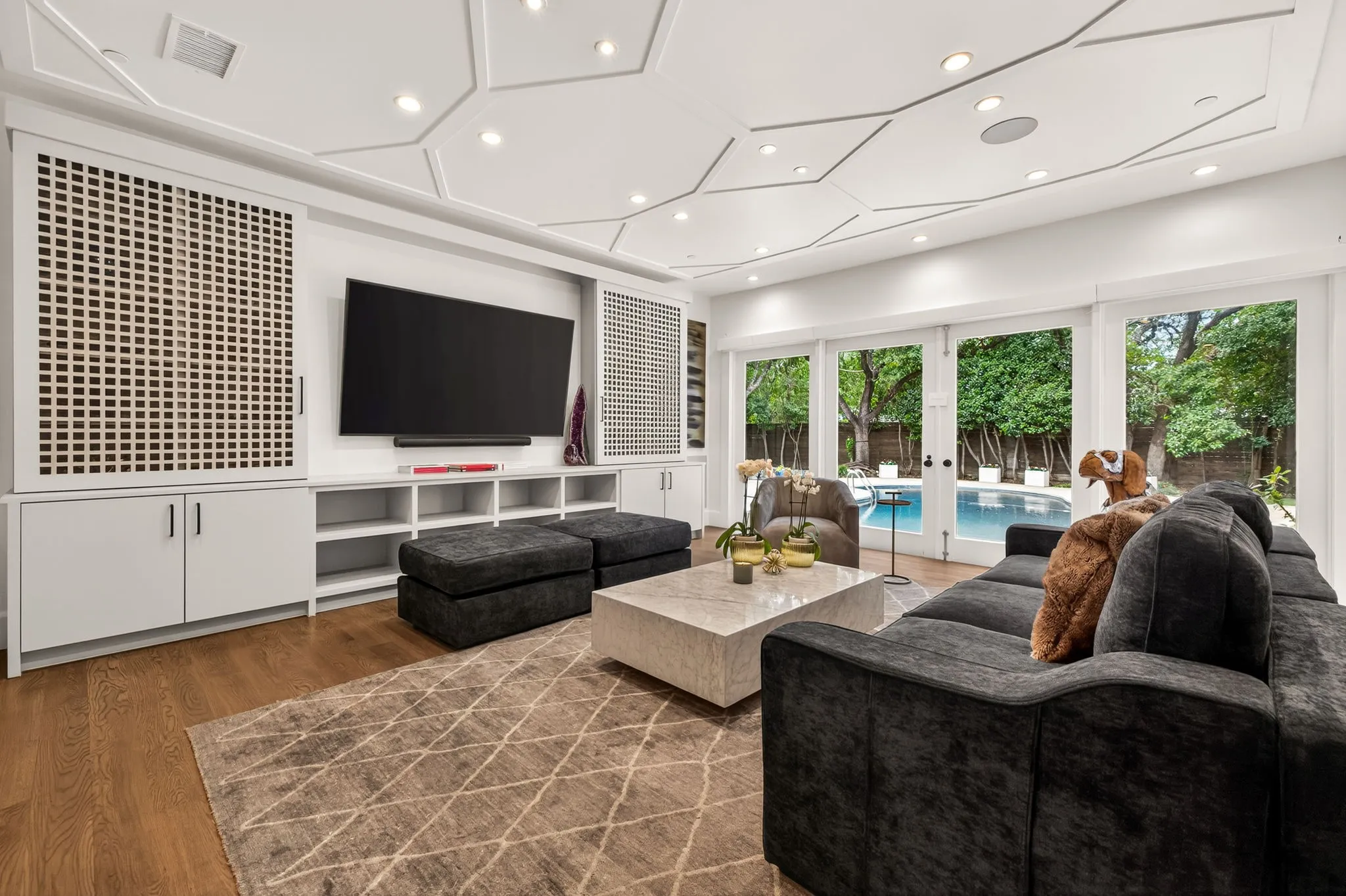 Living area featuring a geometric ceiling design with recessed lighting, built-in entertainment center with integrated shelving, and wood-finish flooring