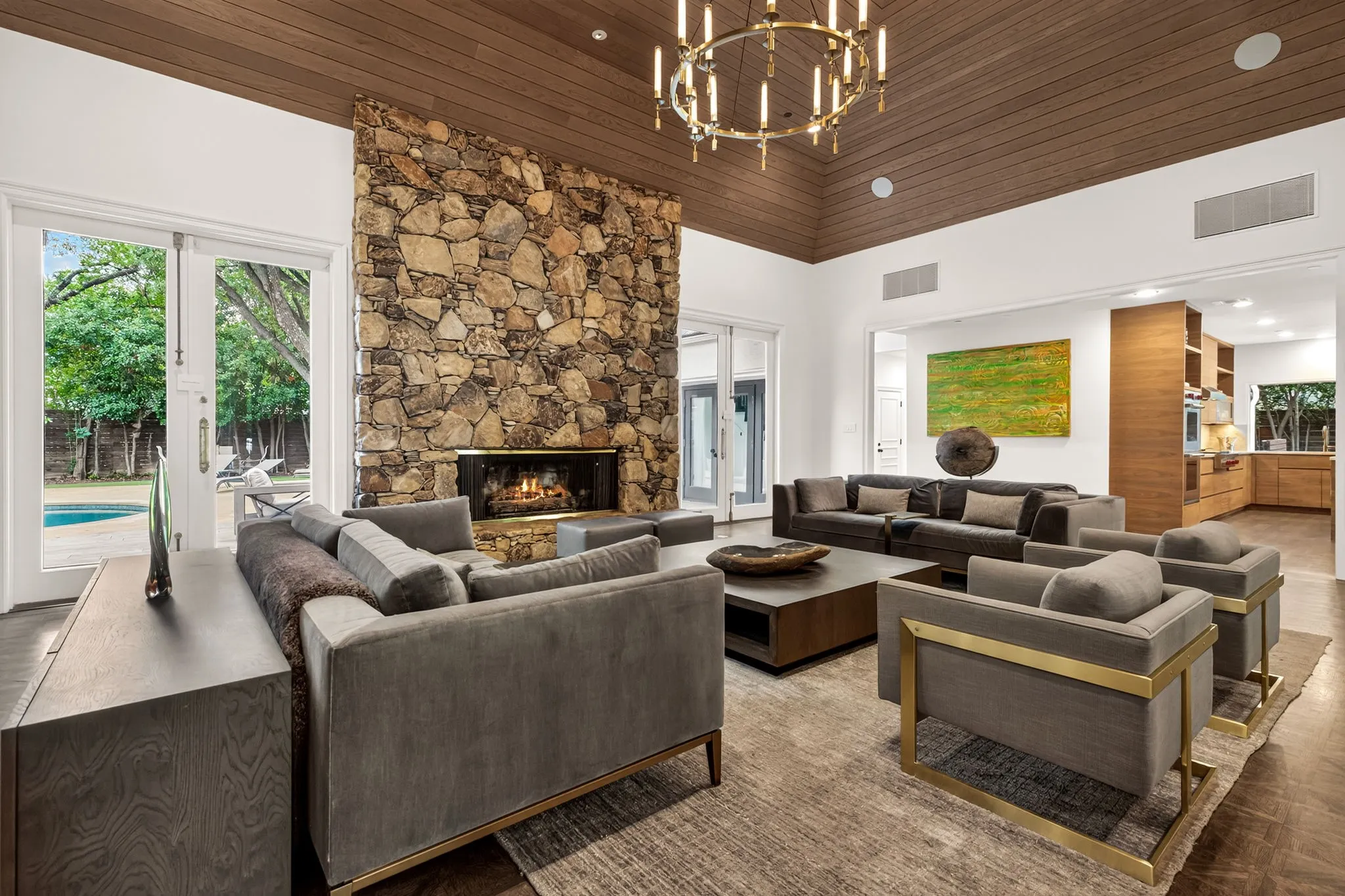 Spacious living area featuring a vaulted wood-paneled ceiling, a floor-to-ceiling stone fireplace, and direct access to the outdoor area with a visible pool