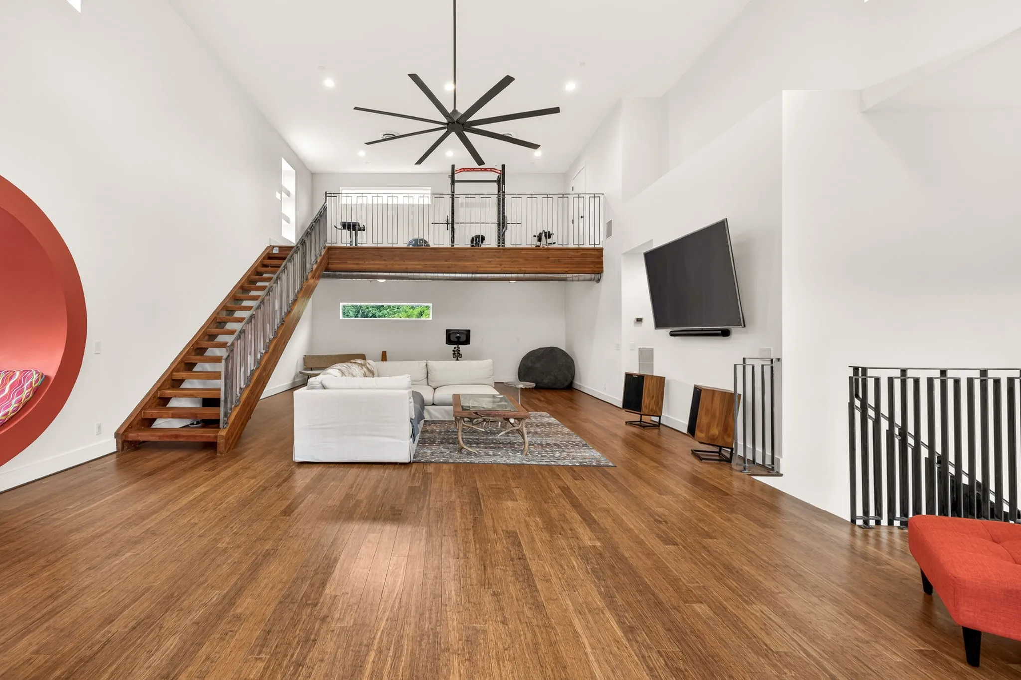 Vaulted ceilings in this spacious room featuring wood-finish flooring, a built-in circular alcove, and a contemporary ceiling fan