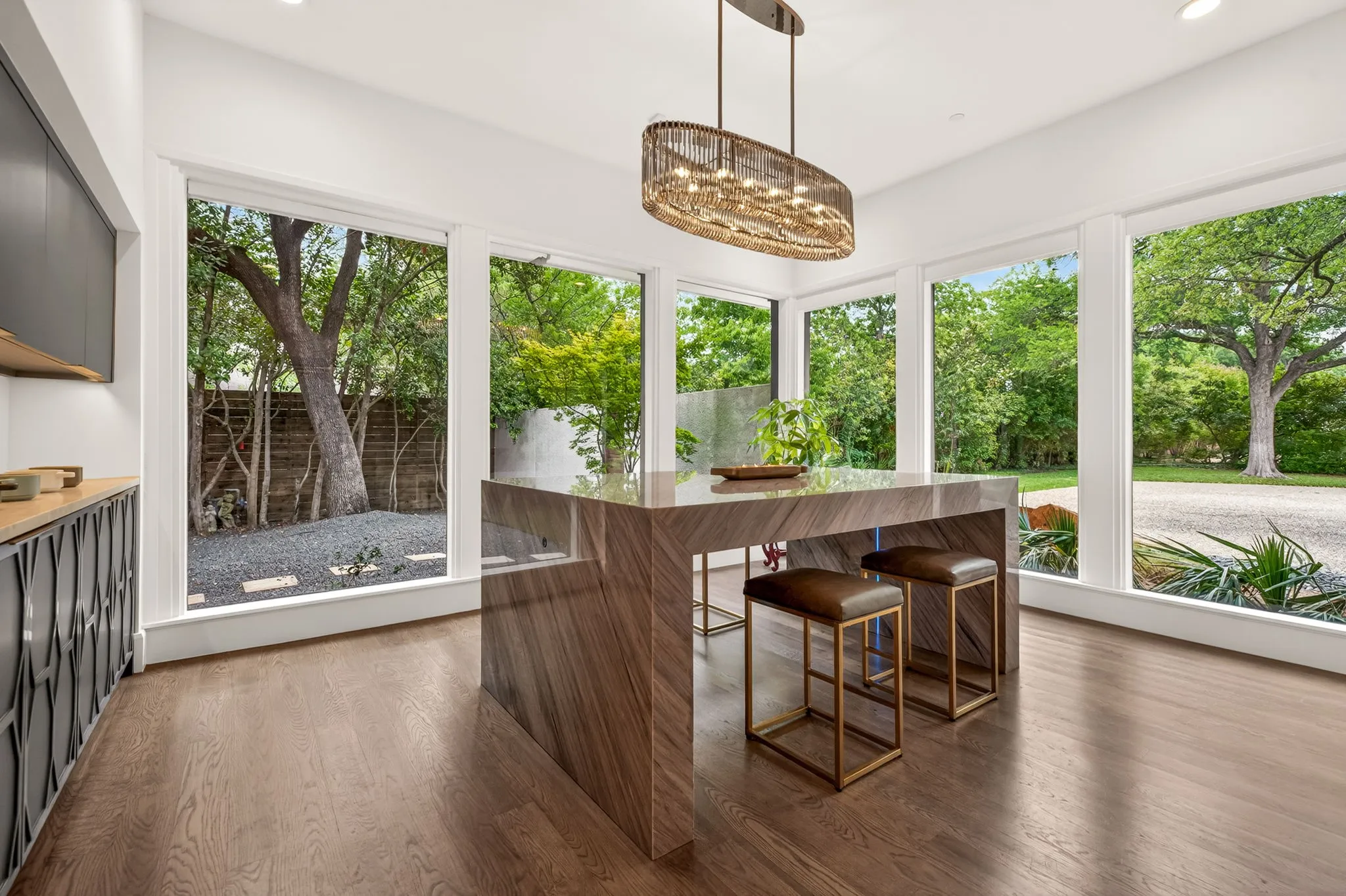 Open-concept kitchen area featuring a large waterfall island with a stone countertop, a modern linear chandelier, and wood-finish flooring
