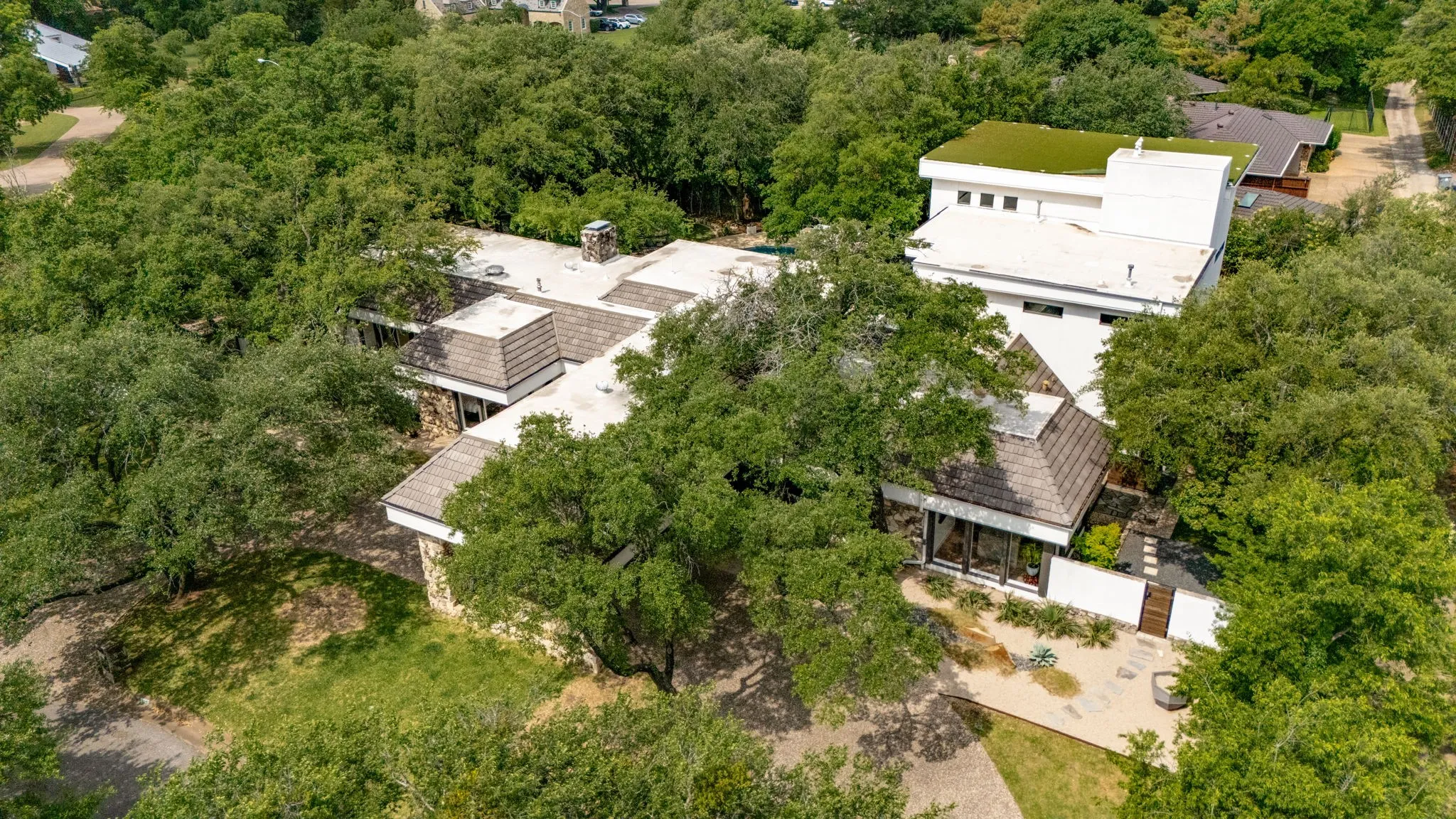 Contemporary architecture featuring extensive flat rooflines, a green roof section, stone accent walls, and mature tree coverage