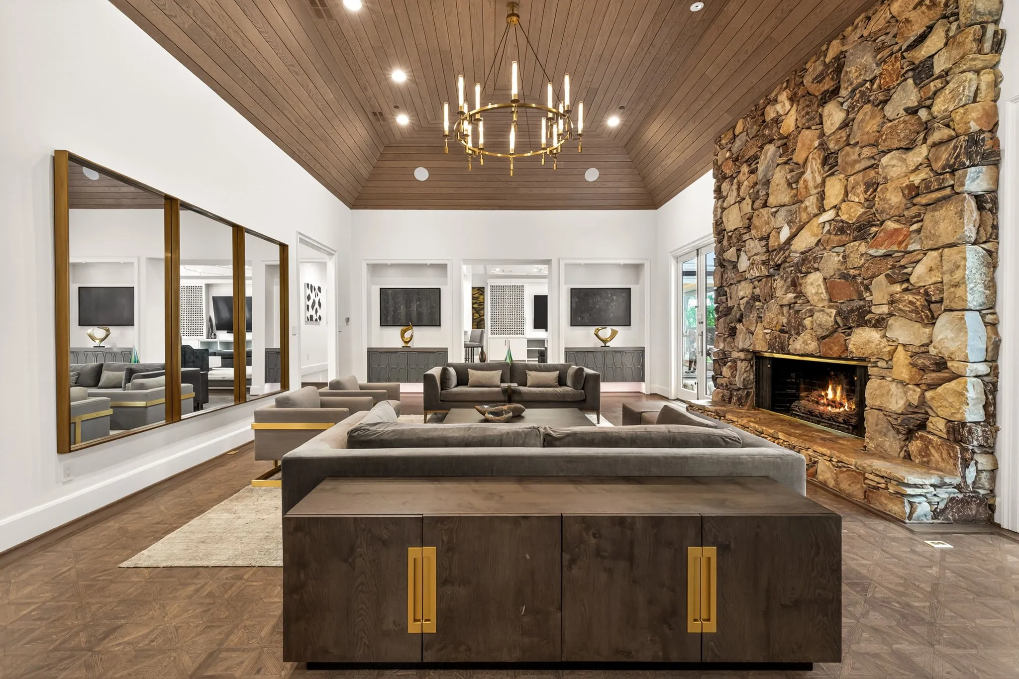 Spacious living area featuring a vaulted wood-paneled ceiling, a large floor-to-ceiling stone fireplace, and wood-finish flooring